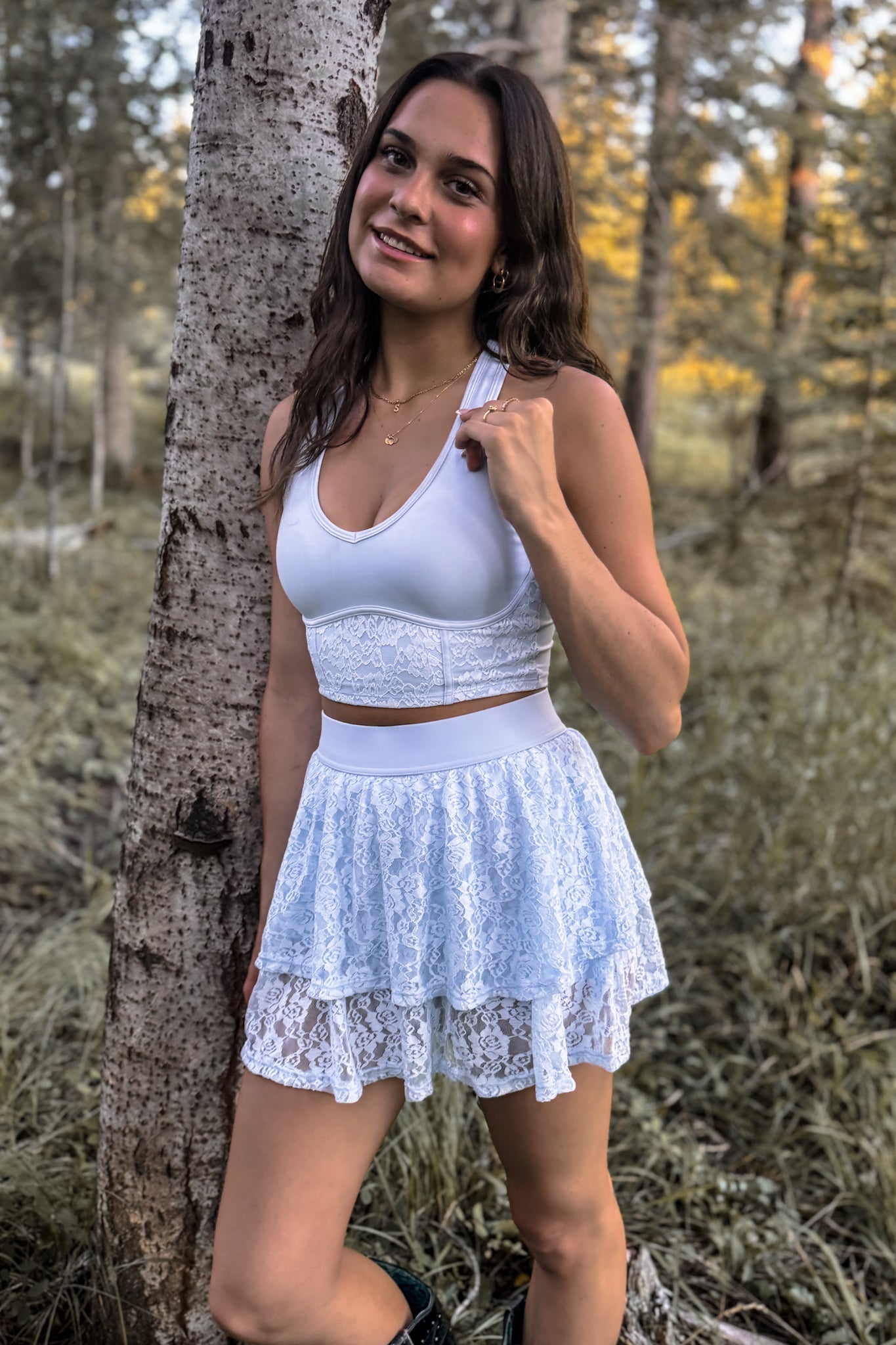 front view of woman wearing a stampede lace active skirt with built-in shorts in light baby blue for festivals and activewear standing against a tree