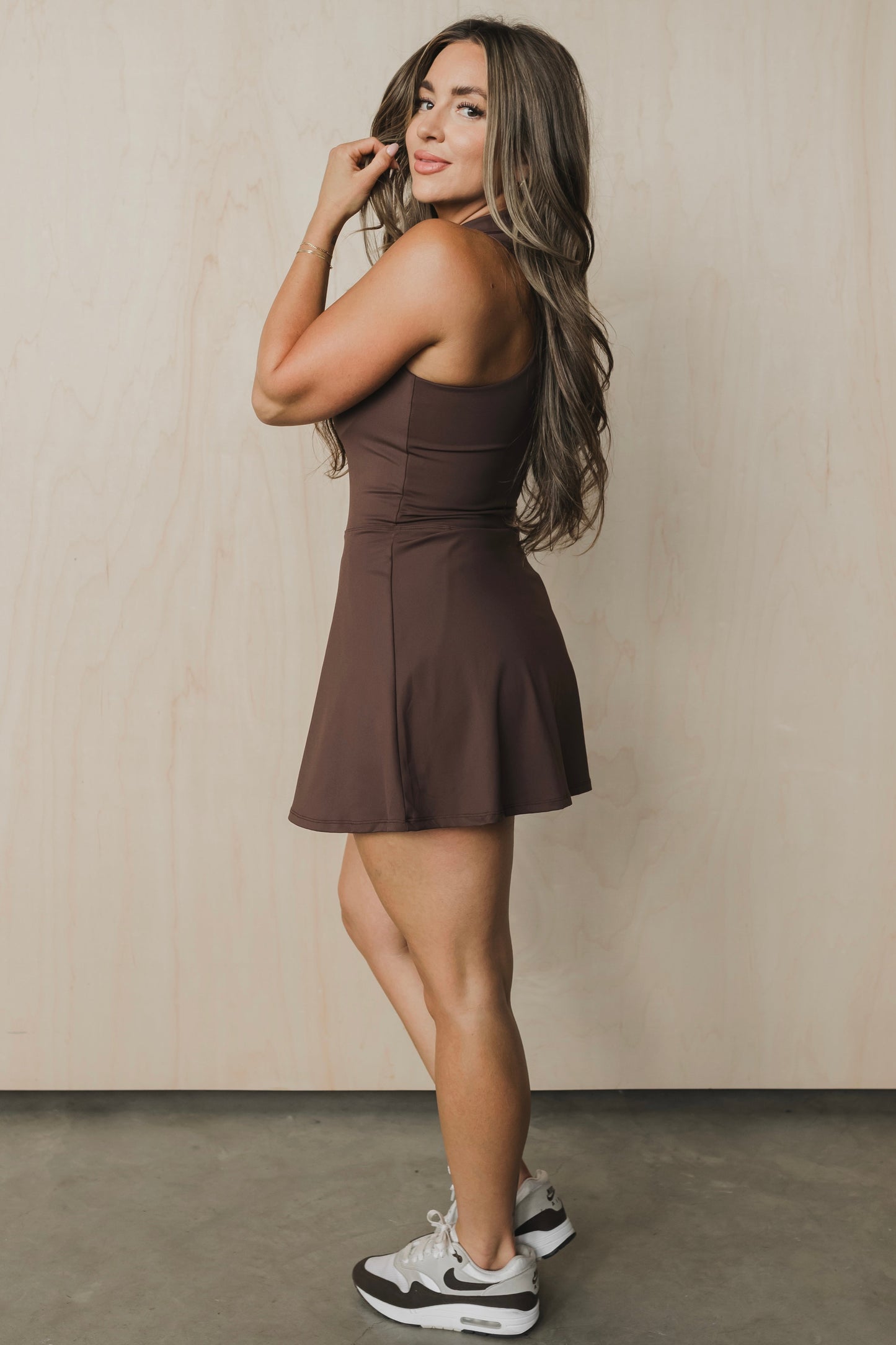 full body side view of woman wearing Tee Time golf dress in brown with built-in shorts and collar for yoga and fitness