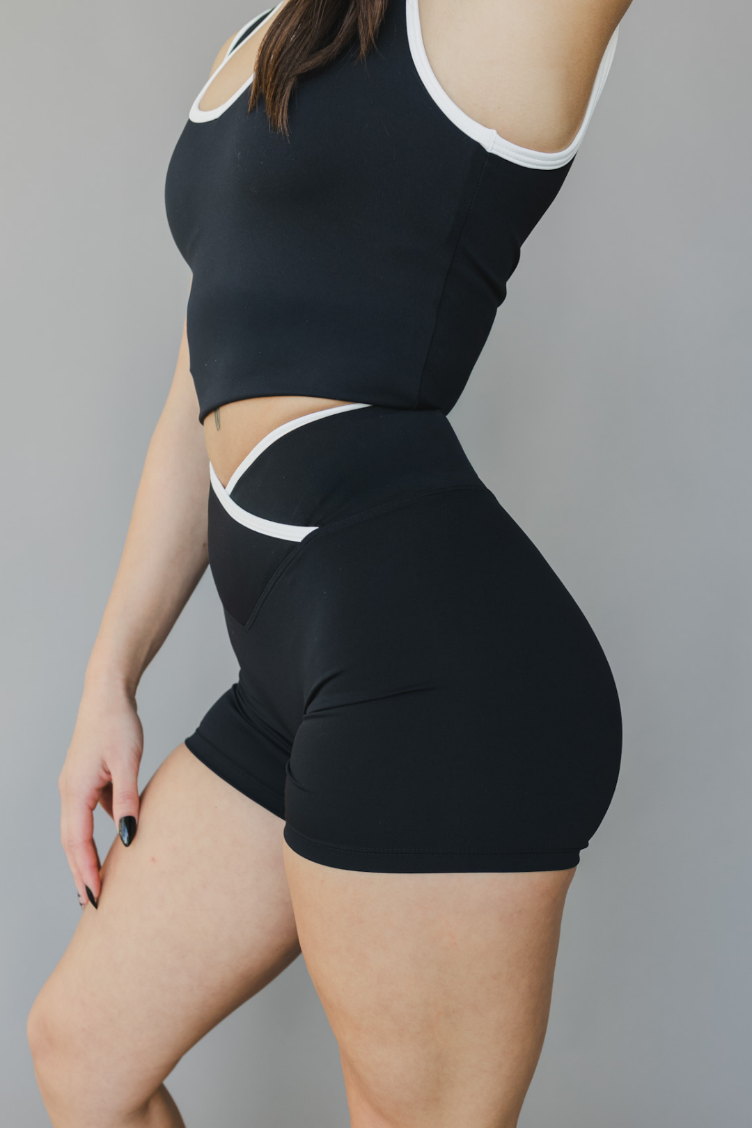 side view of a woman wearing Tina shorts in black with white trim and a matching tank top for athletic wear and loungewear