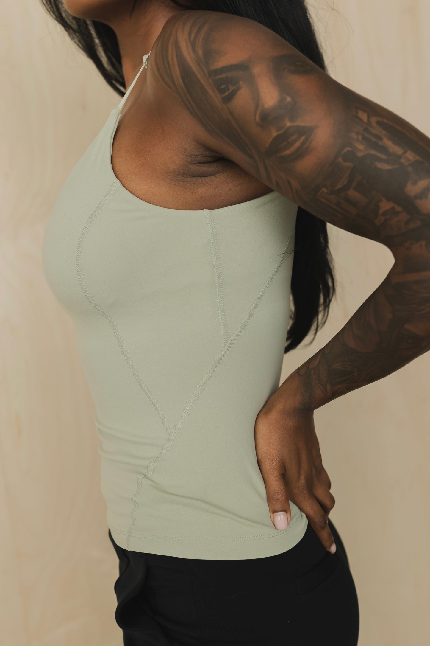 close up back view of a woman wearing a light green tank top with built in bra and lack pants against a beige background