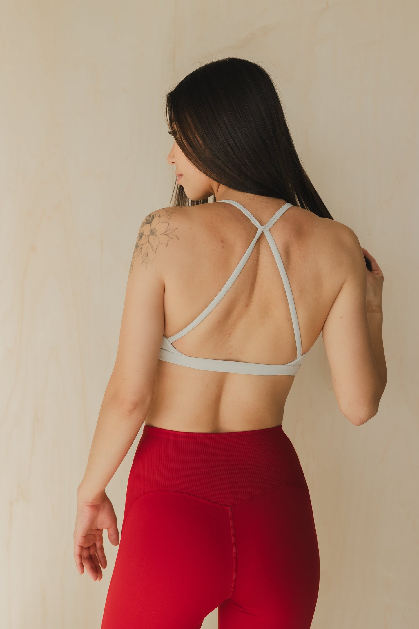 back view of a woman wearing a mini scrunch sports bra in white smoke for pilates and low impact training