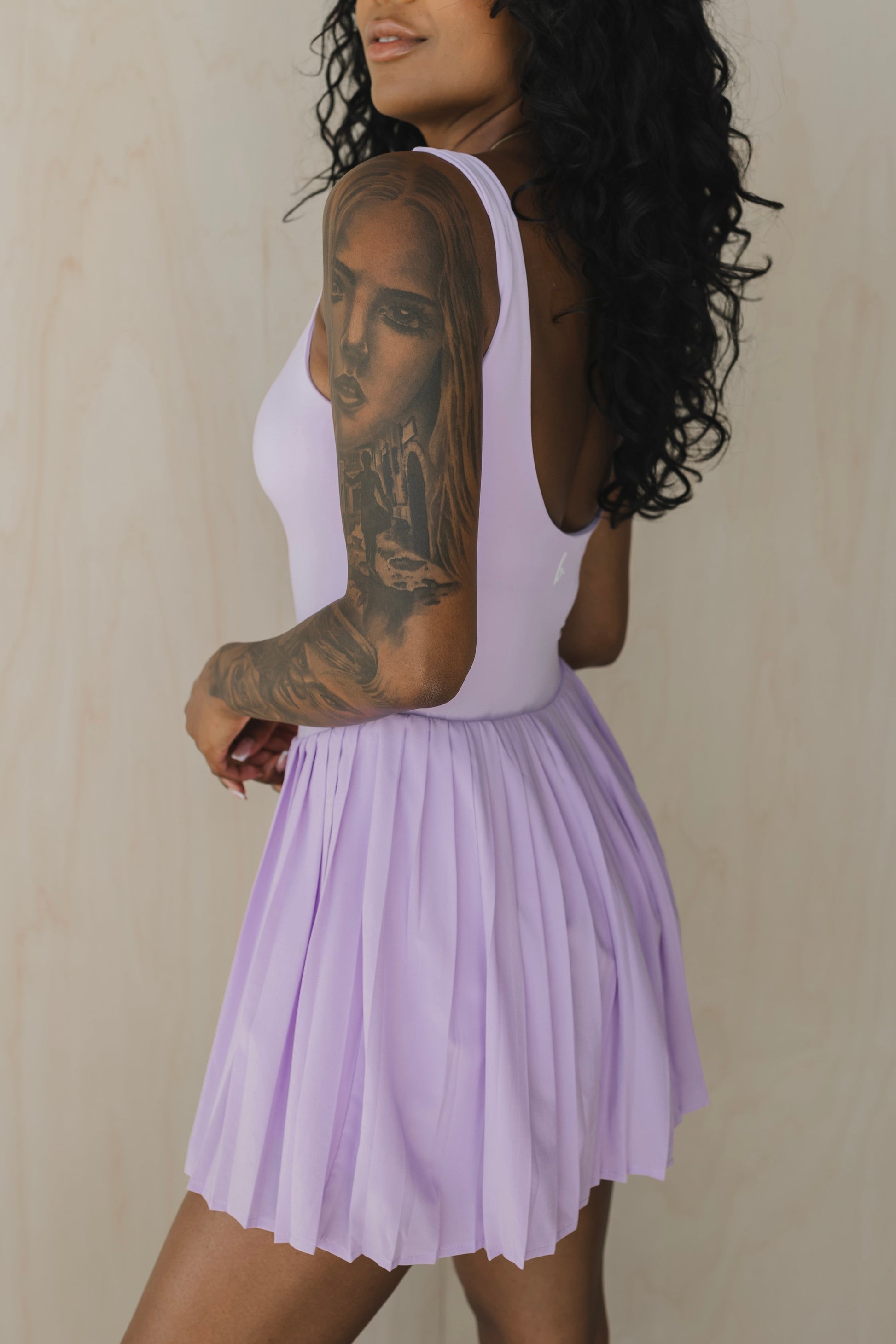 back side view of woman wearing street to Court activewear dress in lilac purple with built-in bra and pocket for tennis and yoga