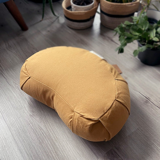 Yellow meditation cushion on a wooden floor with plants in the background