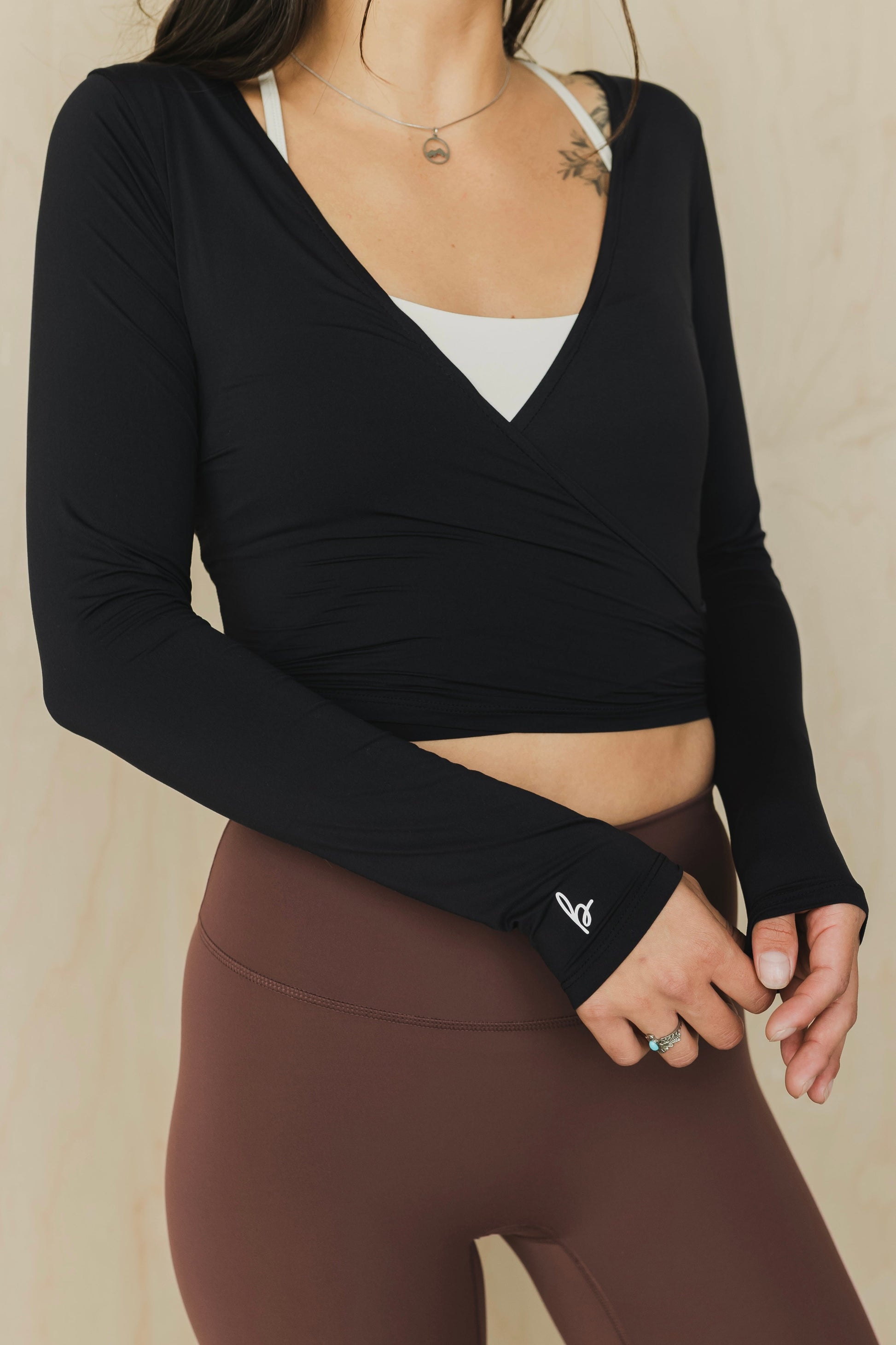 Person wearing a black long-sleeve crop top and brown leggings on a beige background