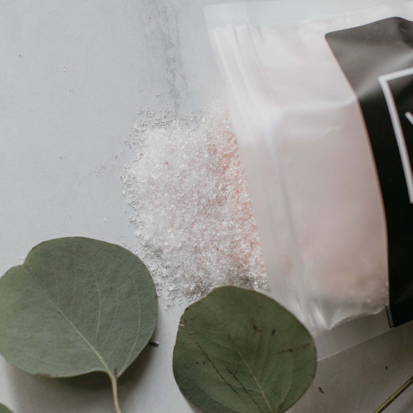 Só Salty Bath Salts on a white surface with green leaves and a black and white container.
