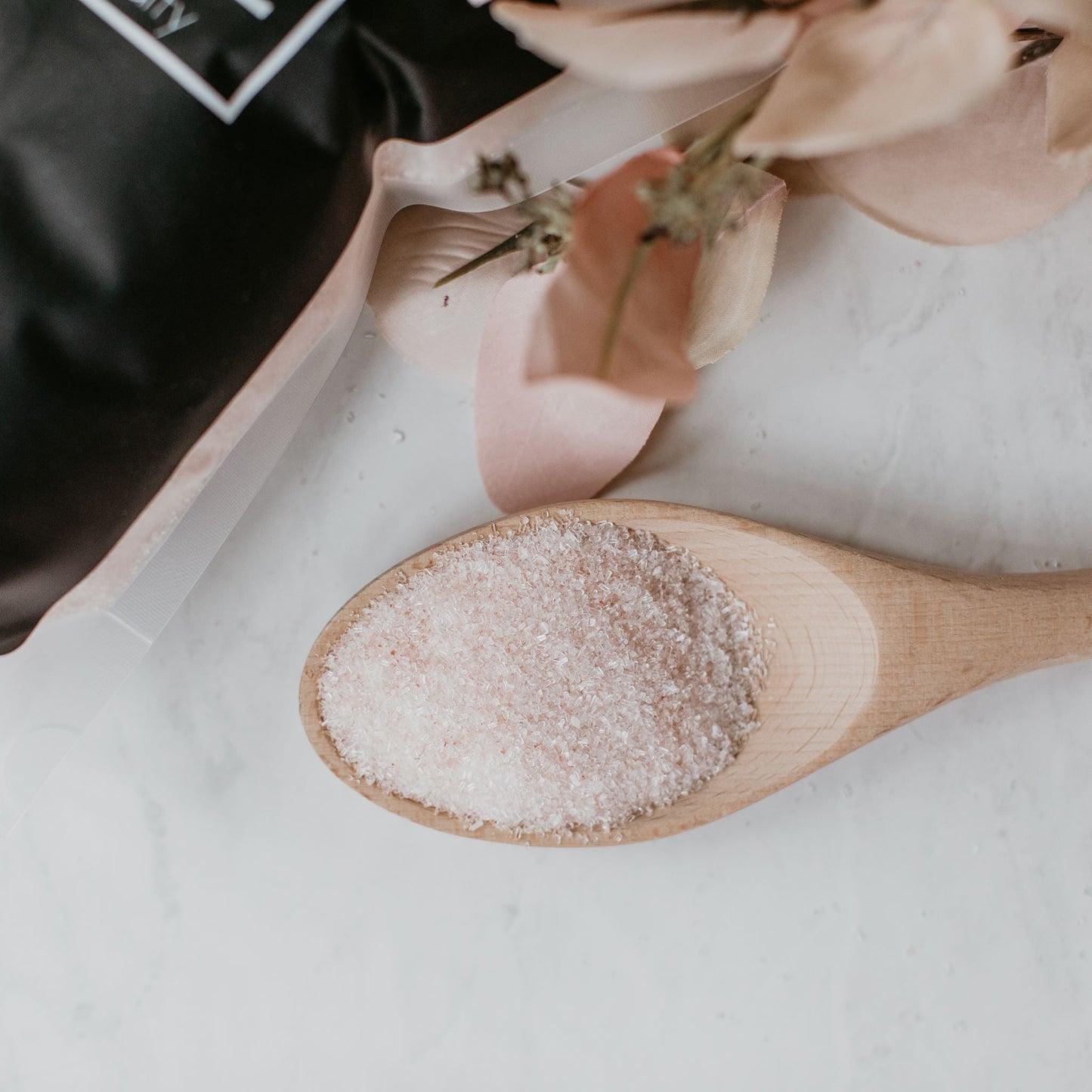 Wooden spoon holding Só Salty Bath Salts on a white surface