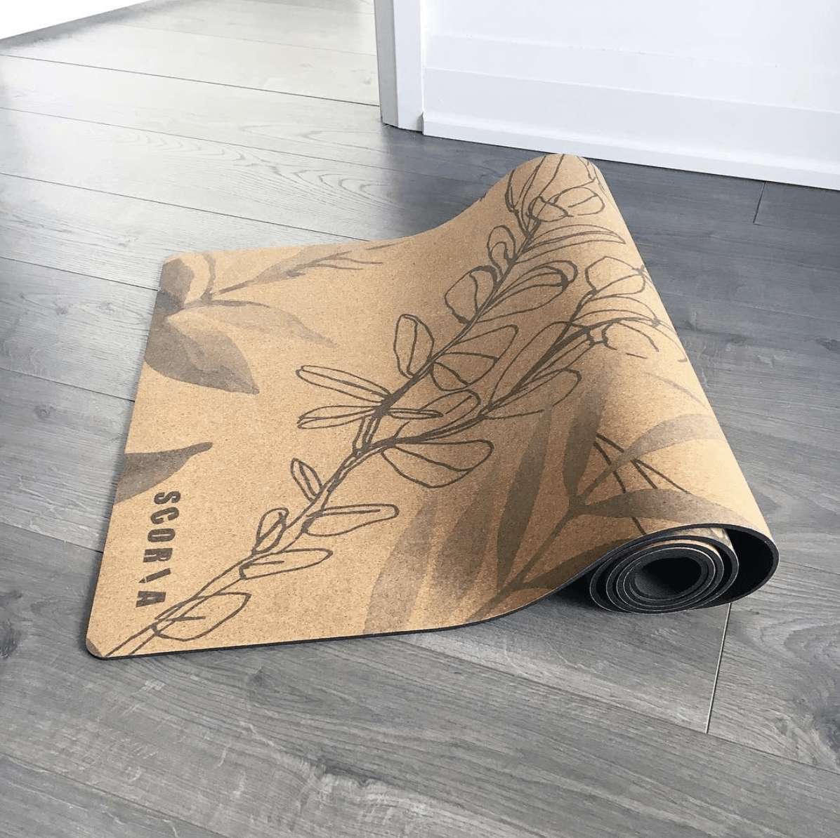 Rolling out cork yoga mat with leaf pattern on a wooden floor