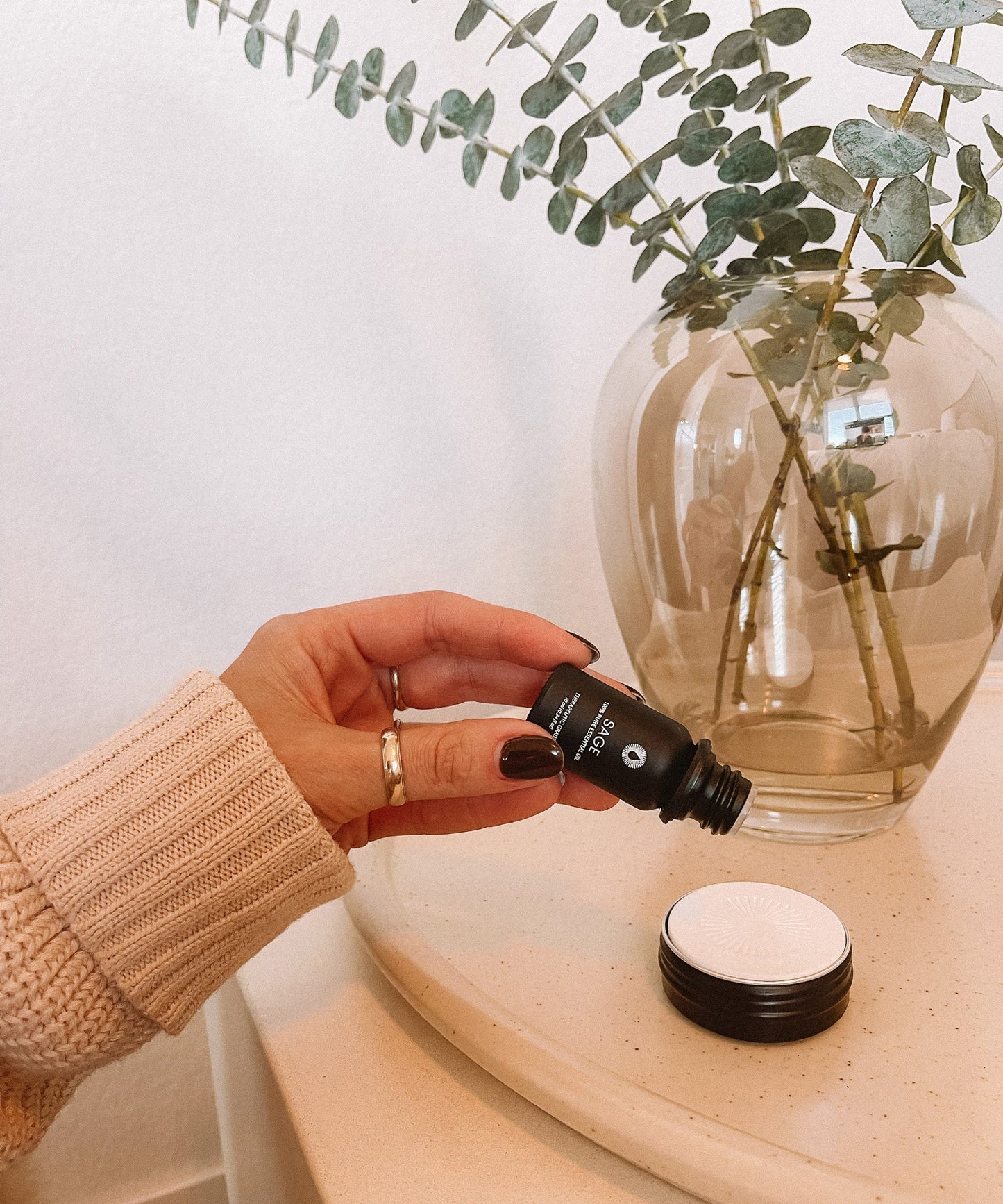 Hand holding a small black bottle with a white cap above a diffusing stone essential oil aromatherapy decor