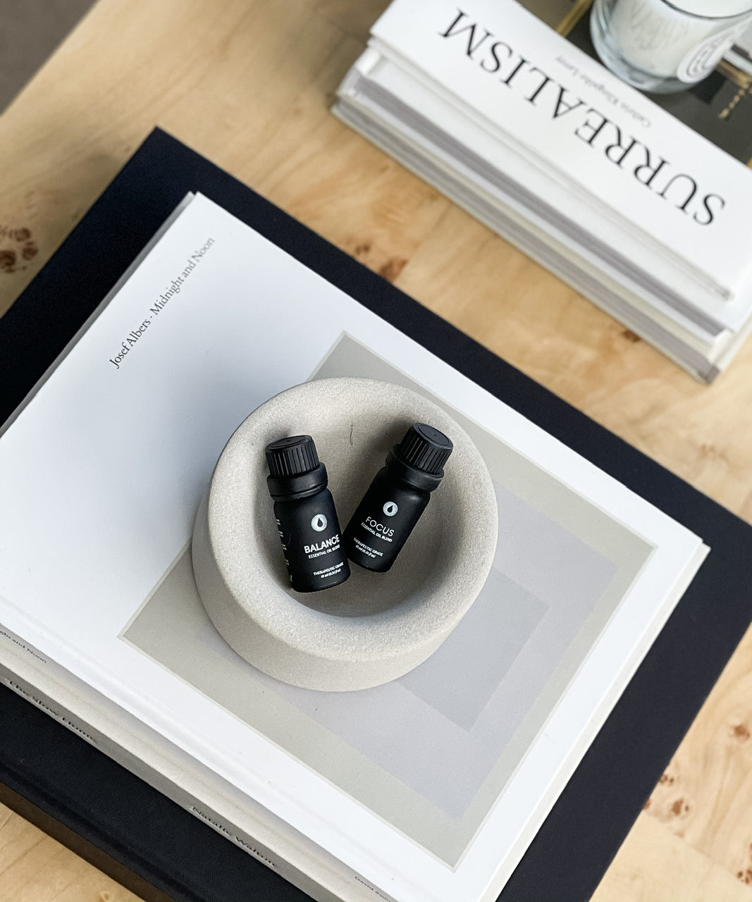 Two black bottles balance essential oil blend aromatherapy in a white bowl on a wooden surface with a book