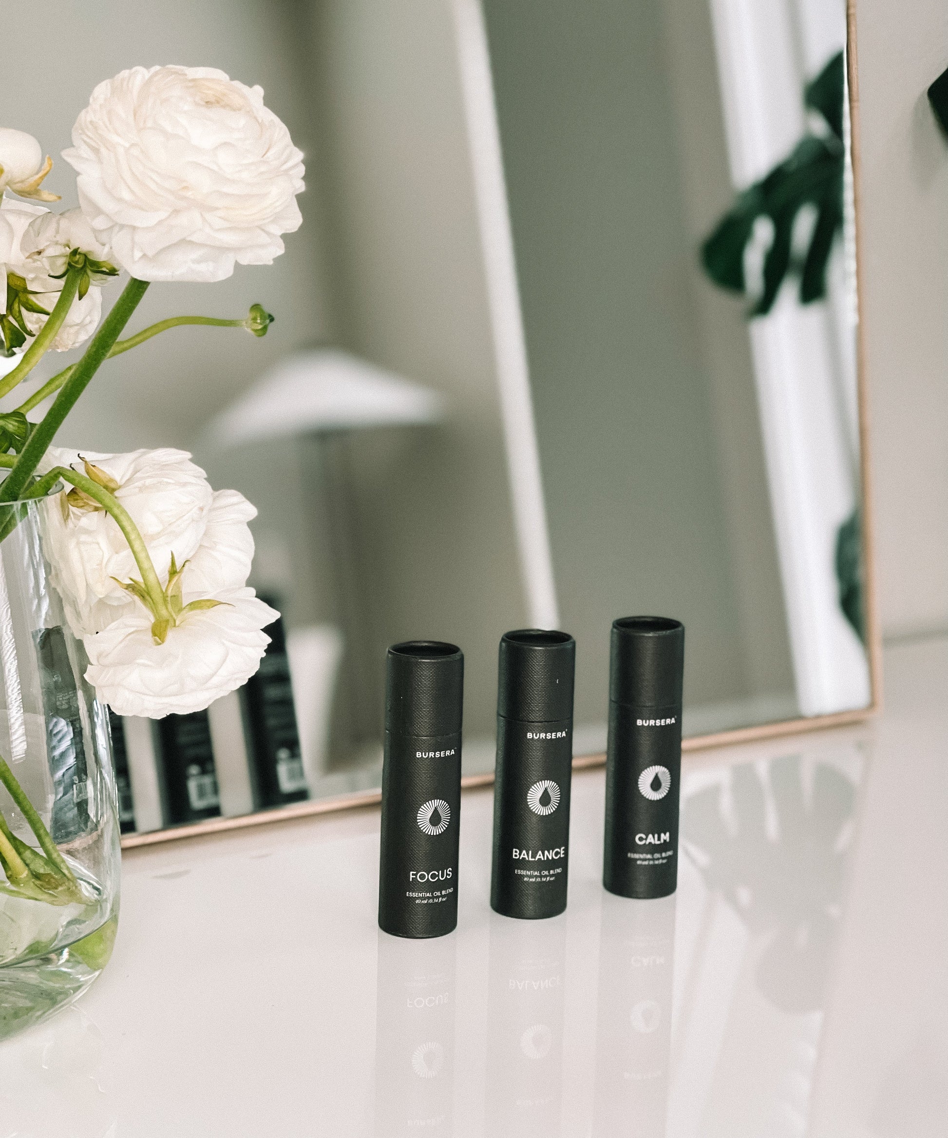 Three black bottles labeled 'Focus', 'Balance', and 'Calm' on a surface with white flowers in the foreground.