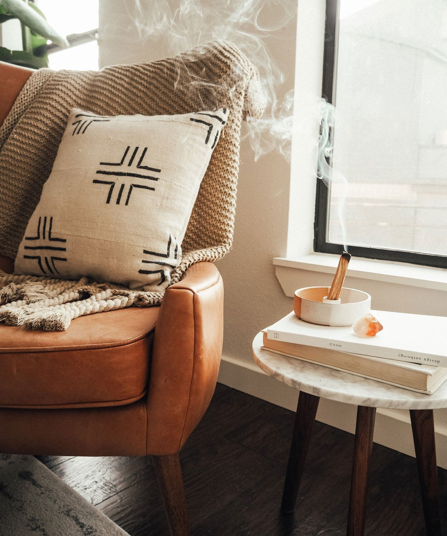 lit palo santo incense sticks aromatherapy along side a brown leather armchair with a patterned pillow and a small table table