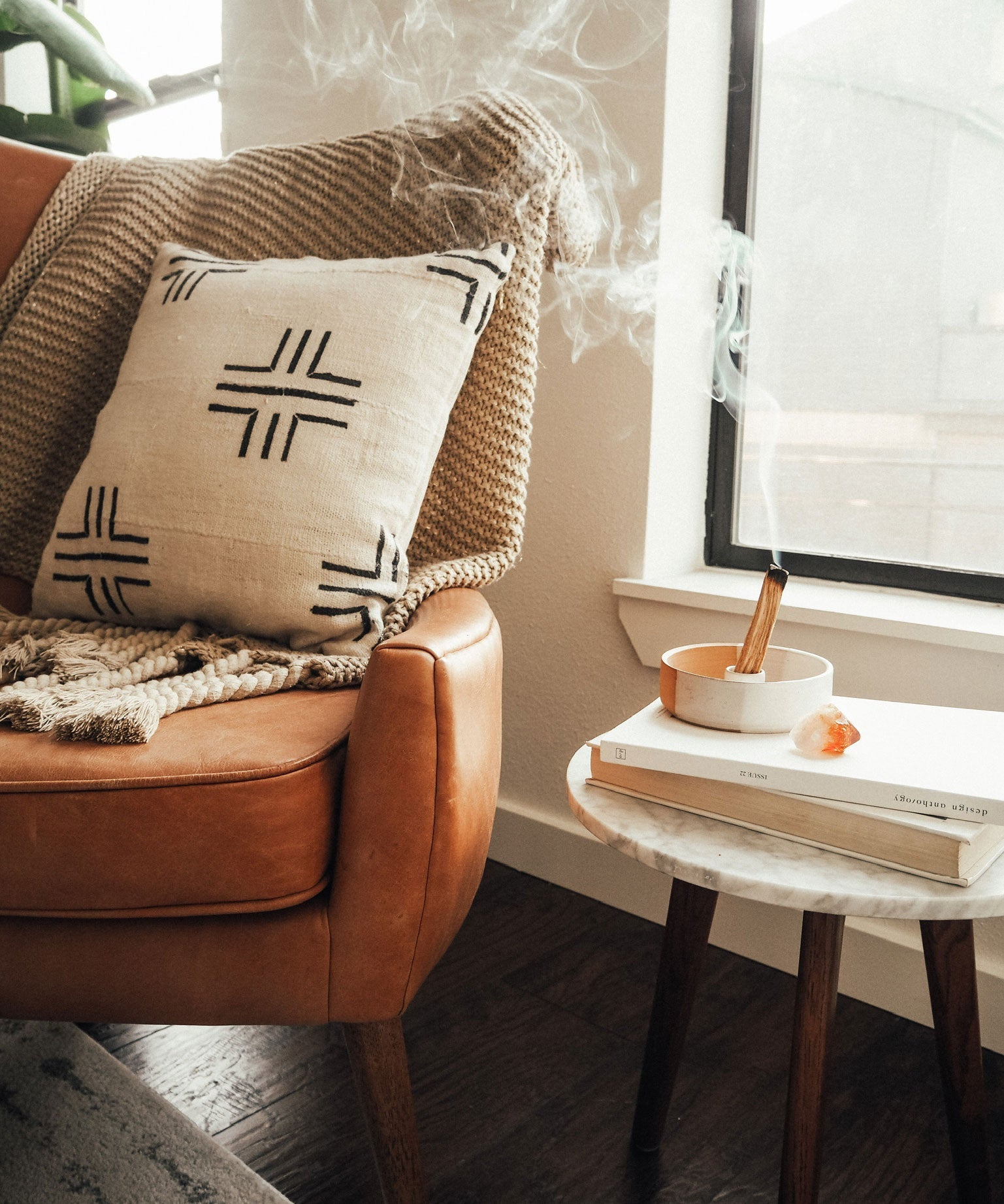 lit palo santo incense sticks aromatherapy along side a brown leather armchair with a patterned pillow and a small table table