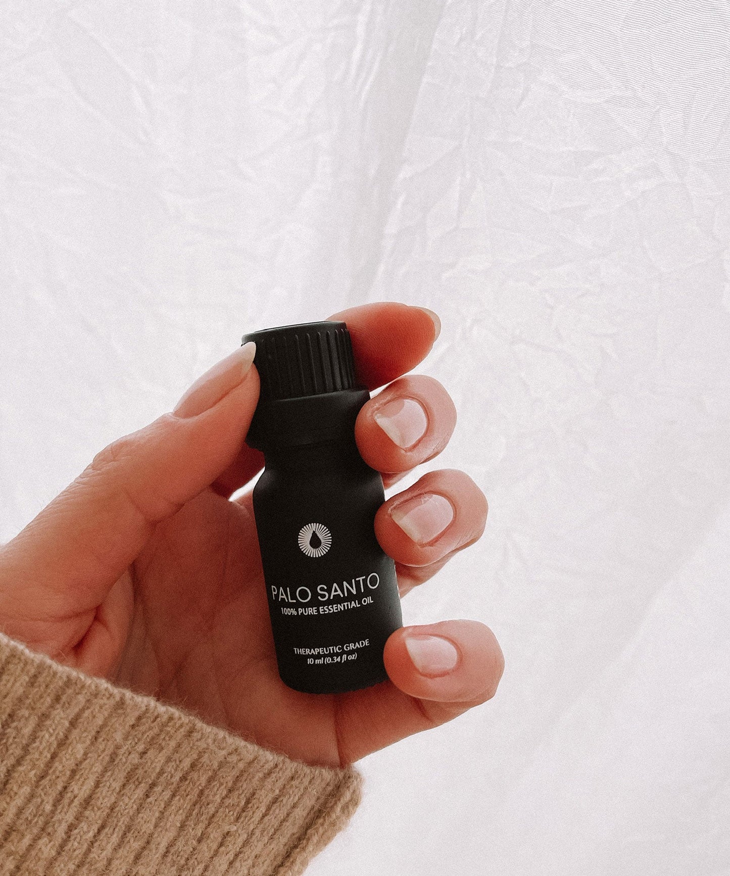 Hand holding a black Palo Santo essential oil bottle against a white background