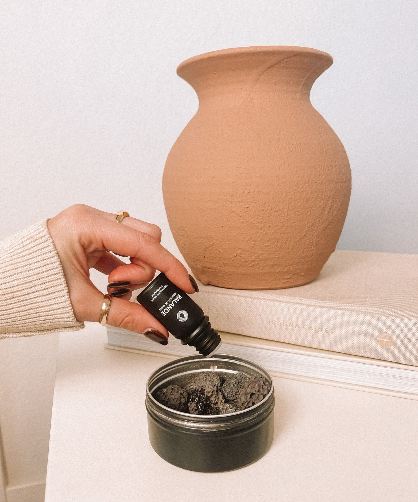 Hand applying a essential oil from a small bottle into a container of volcanic diffusing rocks for essential oil aromatherapy