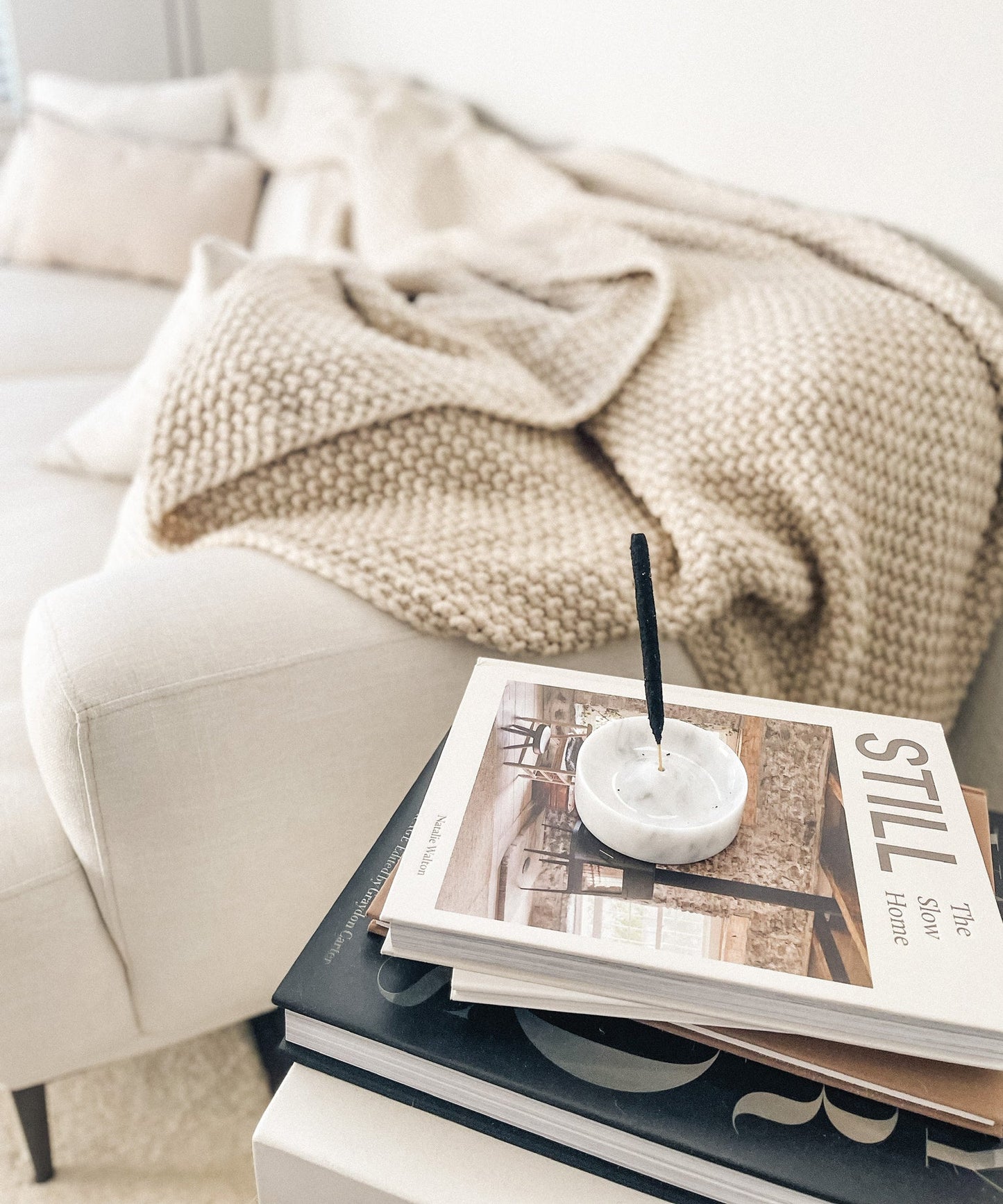 white marble incense holder aromatherapy decor in a white holder on top of a magazine with a beige blanket and pillows in the background