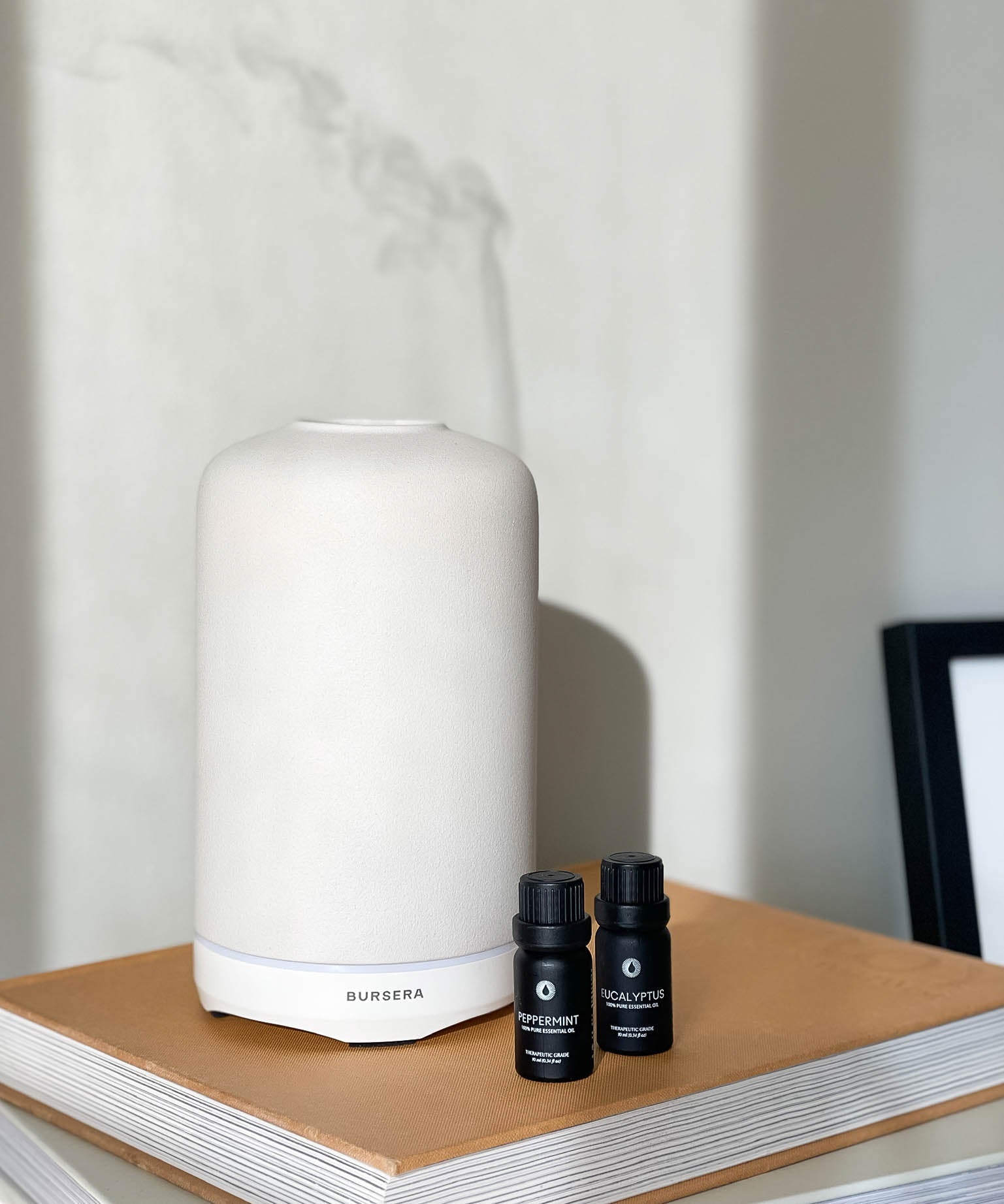 white essential oil diffuser aromatherapy home decor and black essential oil bottles on a wooden surface with a neutral background