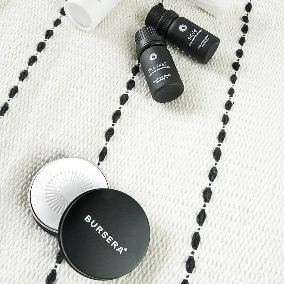 diffusing stone essential oil aromatherapy decor and two black bottles with 'Bursera' branding on a textured white surface.