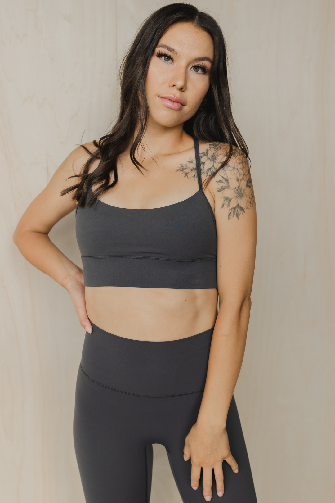 Woman wearing a dark gray sports bra and leggings against a neutral background
