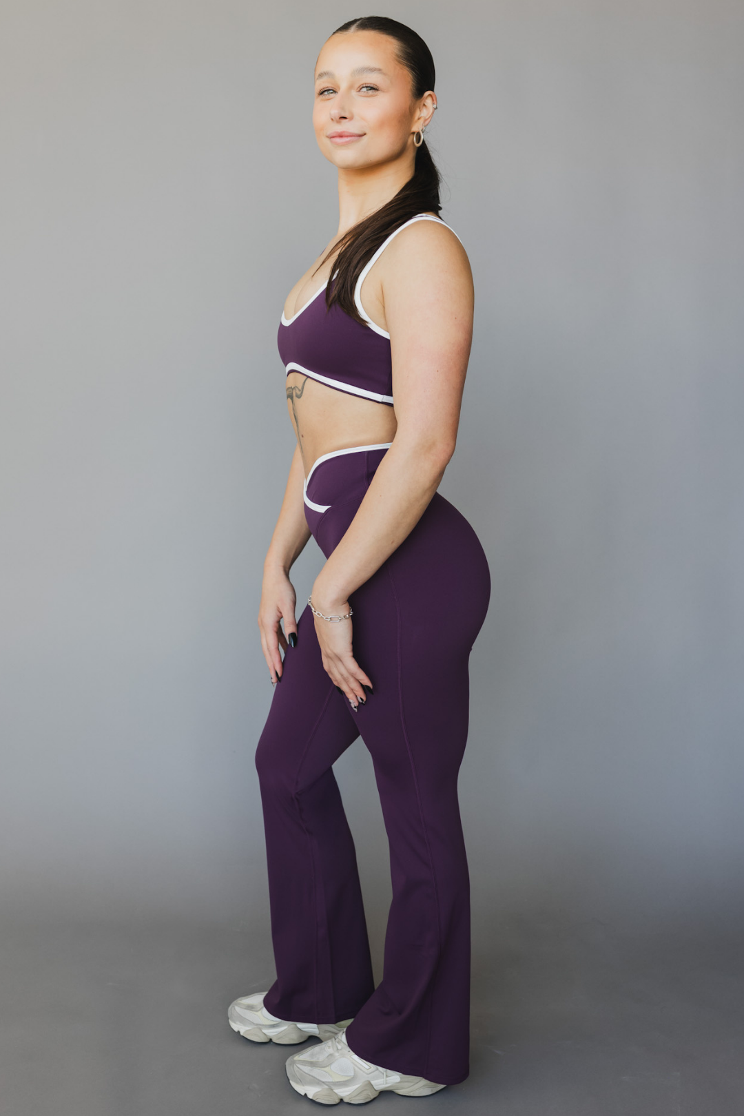full side view of a woman wearing flare leggings in eggplant purple with white trim for workouts and casual athleisure