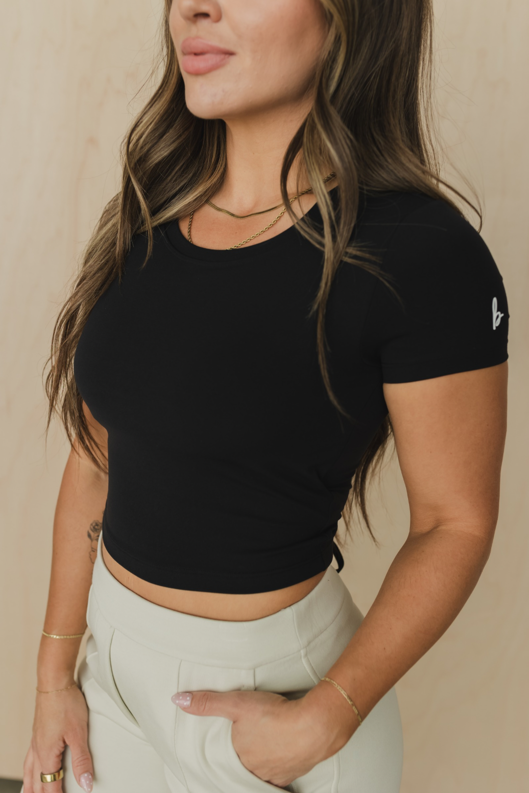 Woman wearing a black crop top and light pants against a beige background