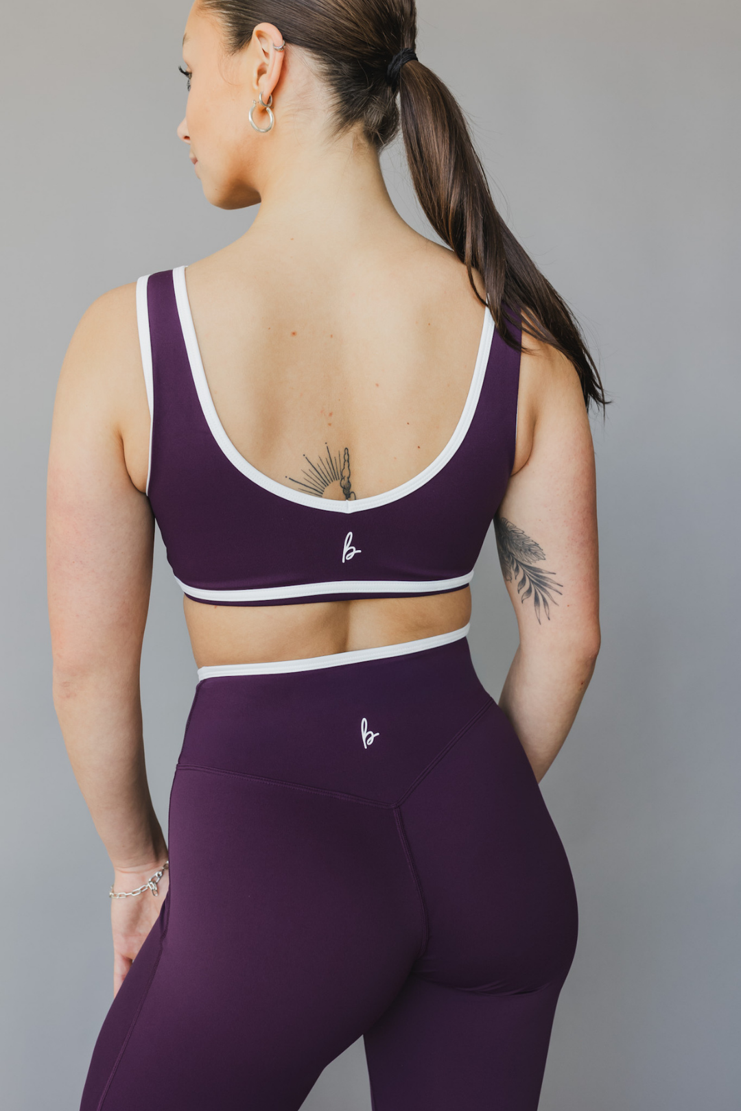 back view of a woman wearing a tina sports bra with white trim and scoop neckline in eggplant purple for yoga and fitness