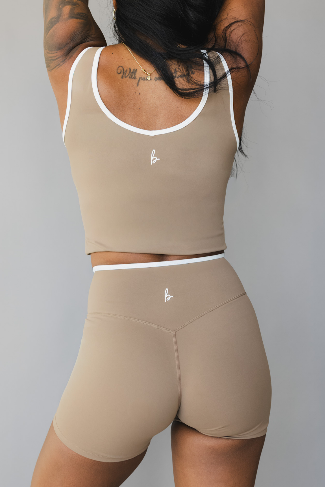 back view of a person wearing a tan color athletic tank top with white trim and matching shorts on a gray background