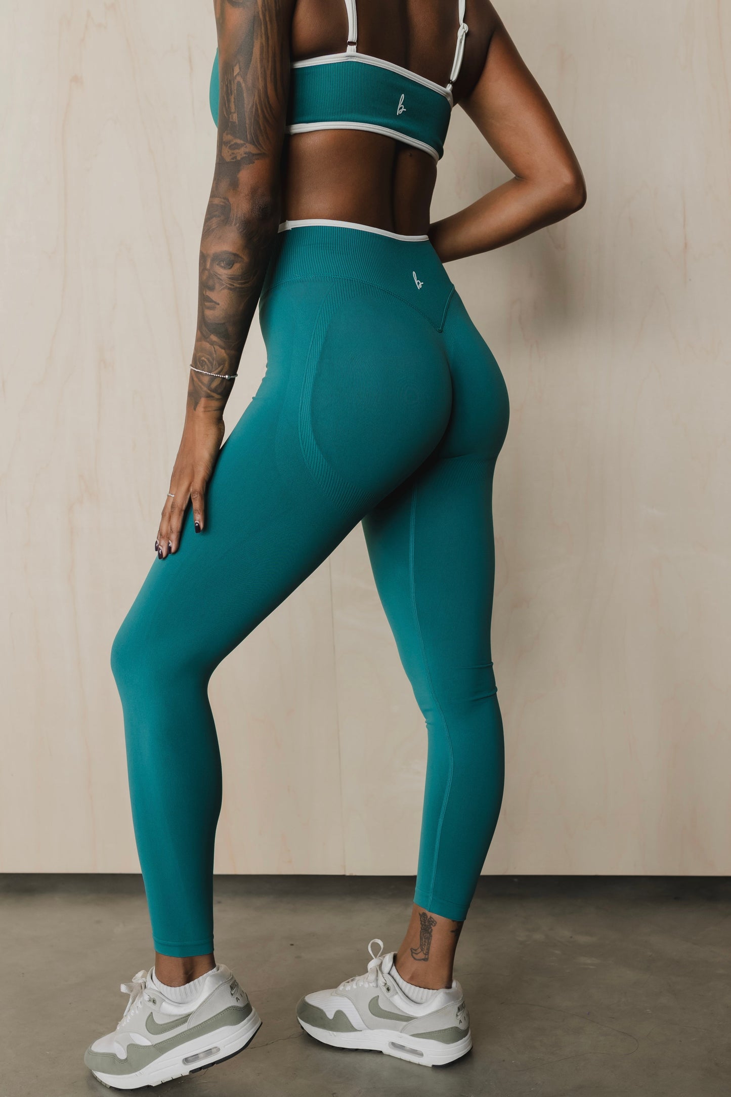 side back view of a woman wearing booty lift sculpt leggings in teal for the gym and high performance training