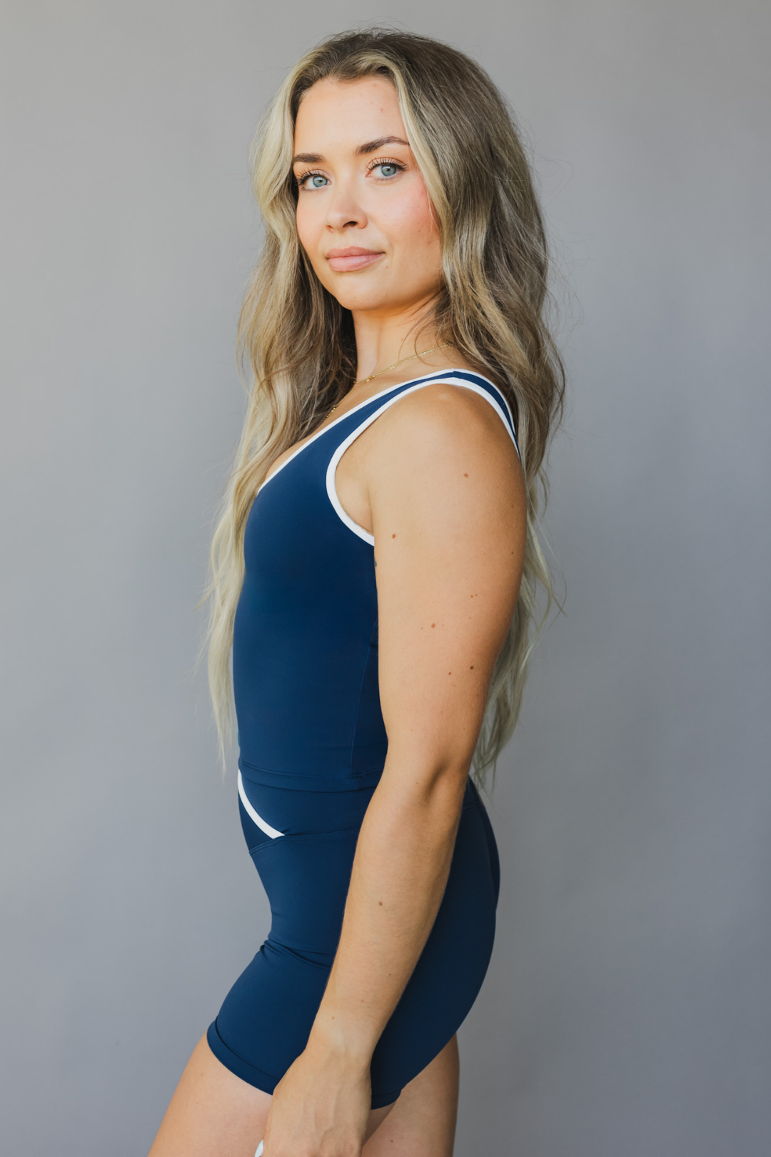 side view of a person wearing a blue color athletic tank top with white trim and matching shorts on a gray background