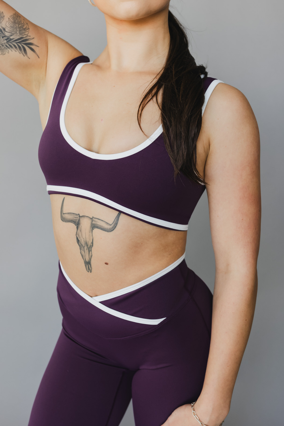 front view of a woman wearing a tina sports bra with white trim and scoop neckline in eggplant purple for yoga and fitness