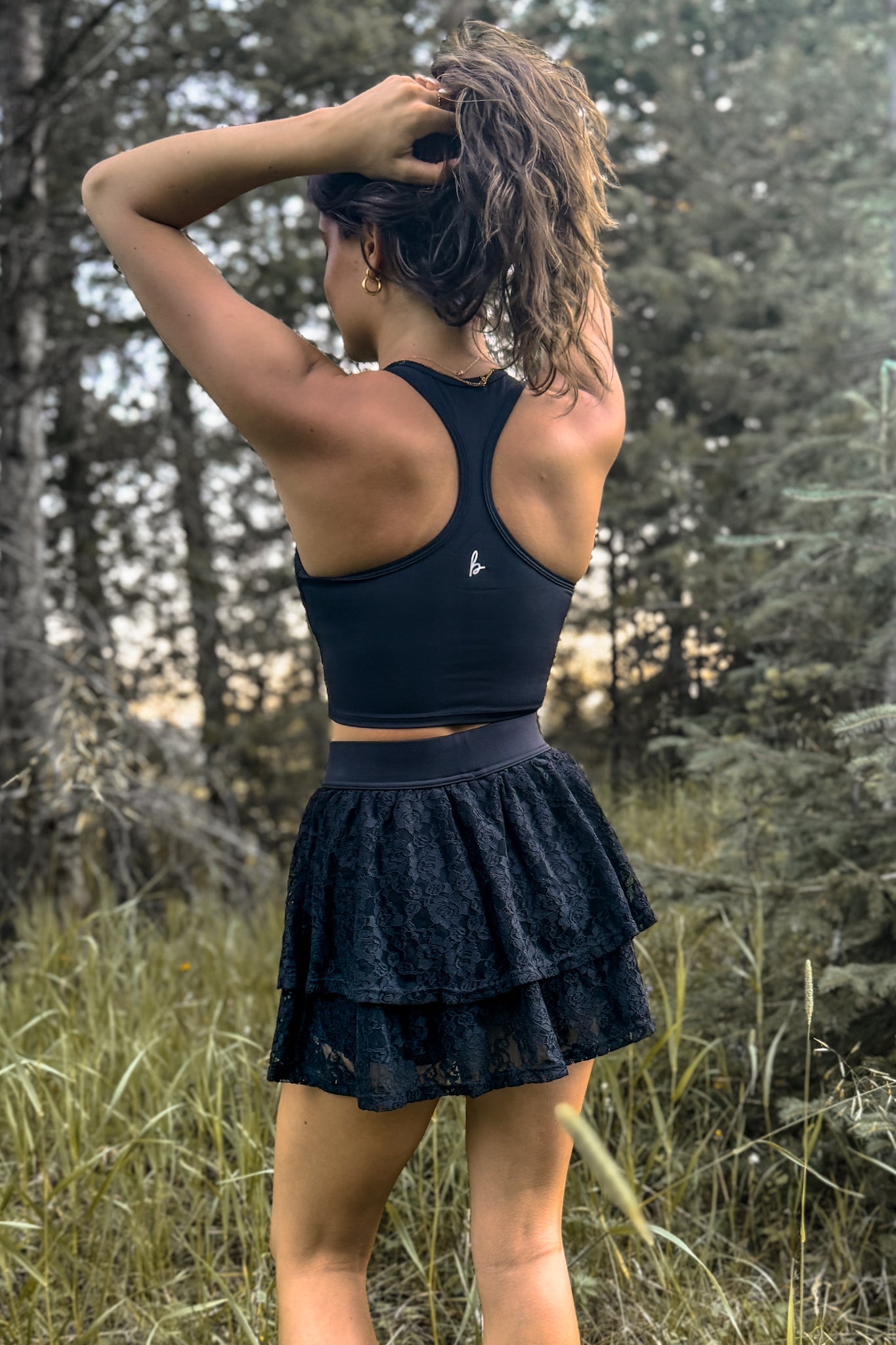 back view of woman wearing a stampede lace active skirt with built-in shorts in black for festivals and activewear