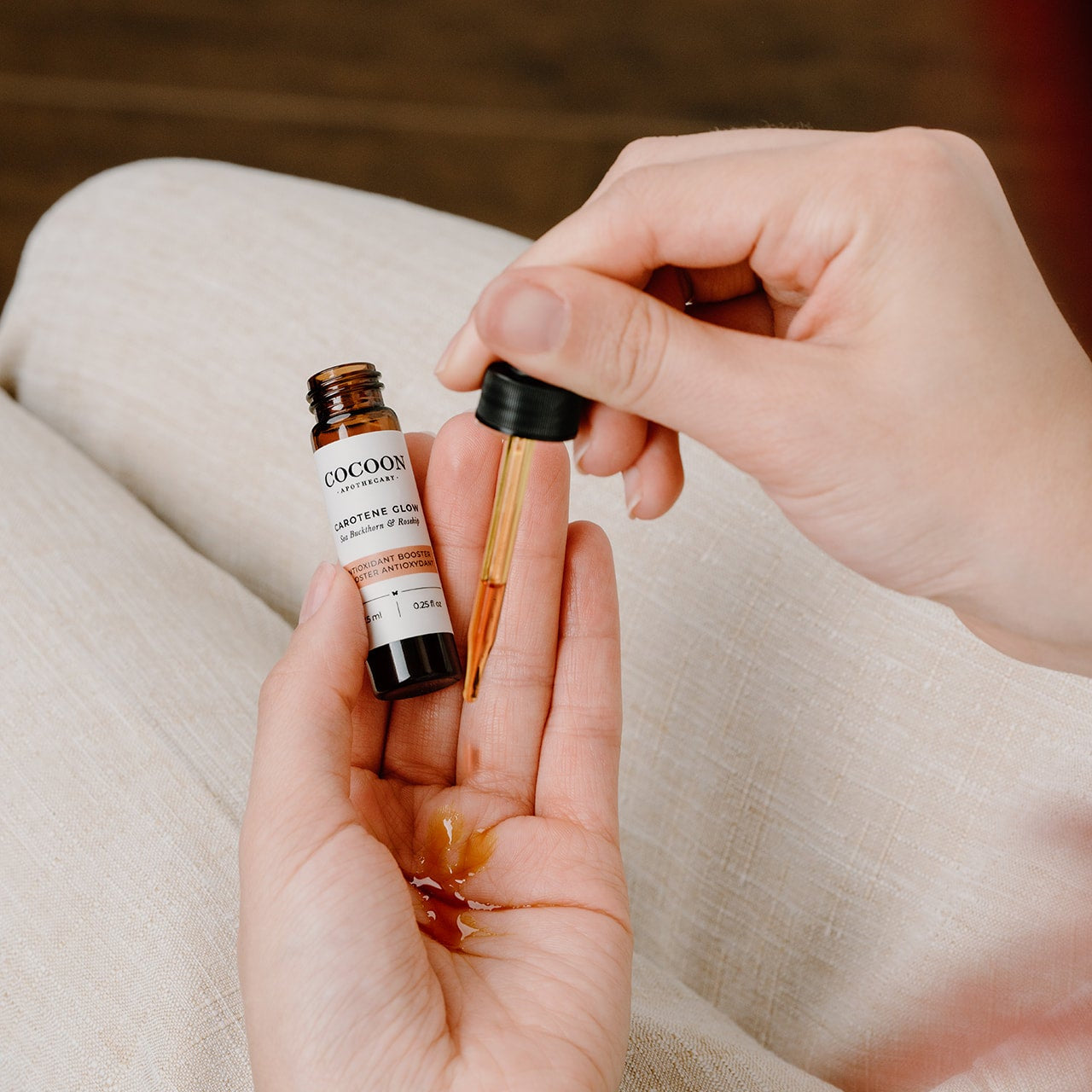 Person holding a small bottle of Cocoon Carotene Glow Antioxidant Booster skincare product with a blurred background