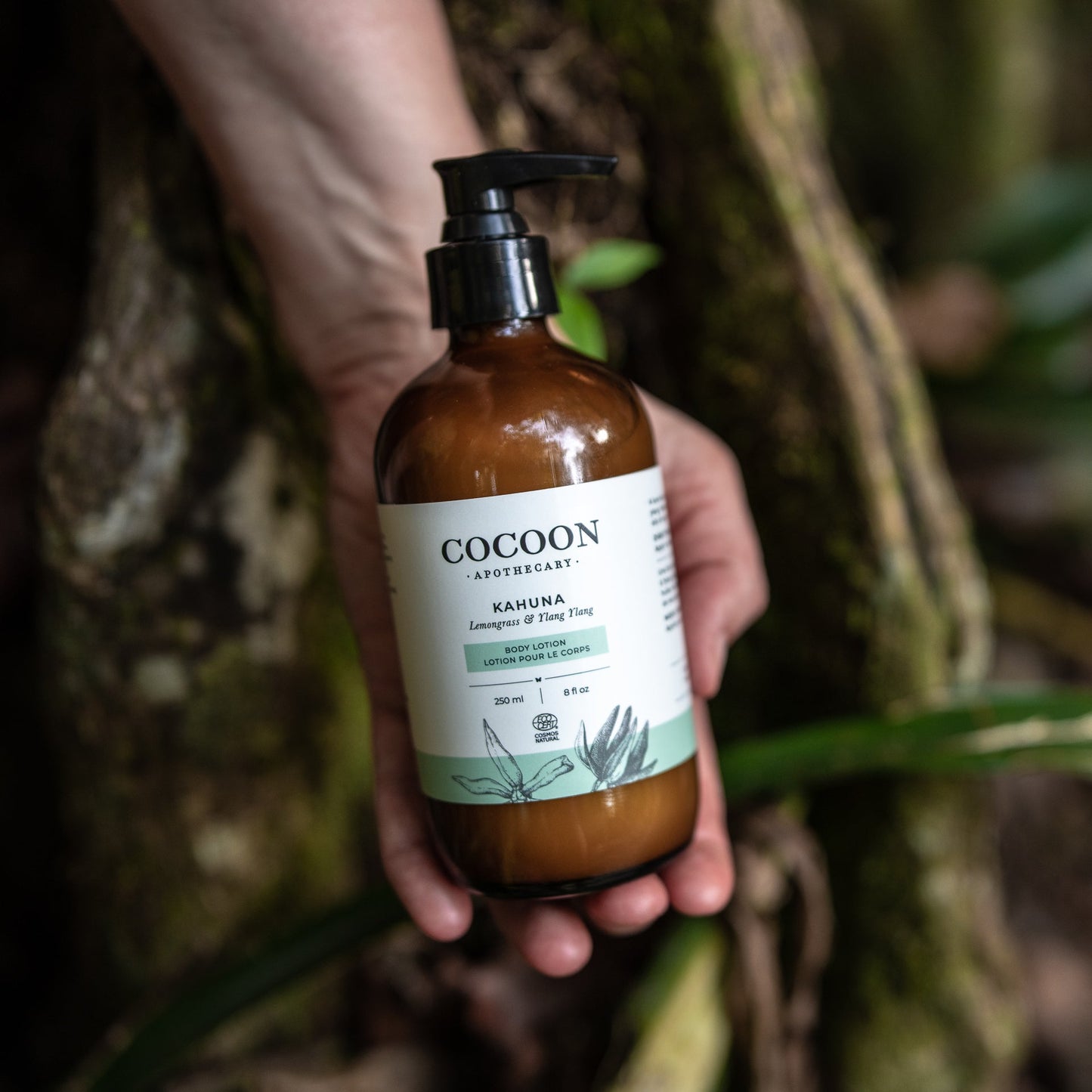 Hand holding a bottle of Cocoon body lotion against a natural background