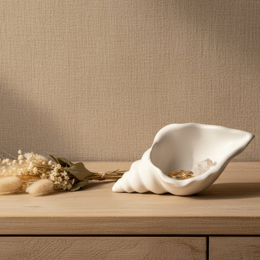 Matte white conch shell shaped jesmonite trinket tray and jewelry dish styled on a bedroom dresser with gold rings, crystals, and dried florals in warm natural light