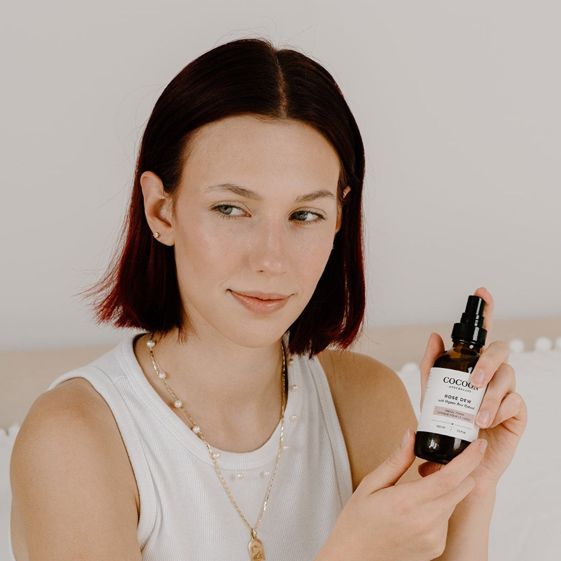 Woman holding a bottle of Rose Dew facial toner against a neutral background