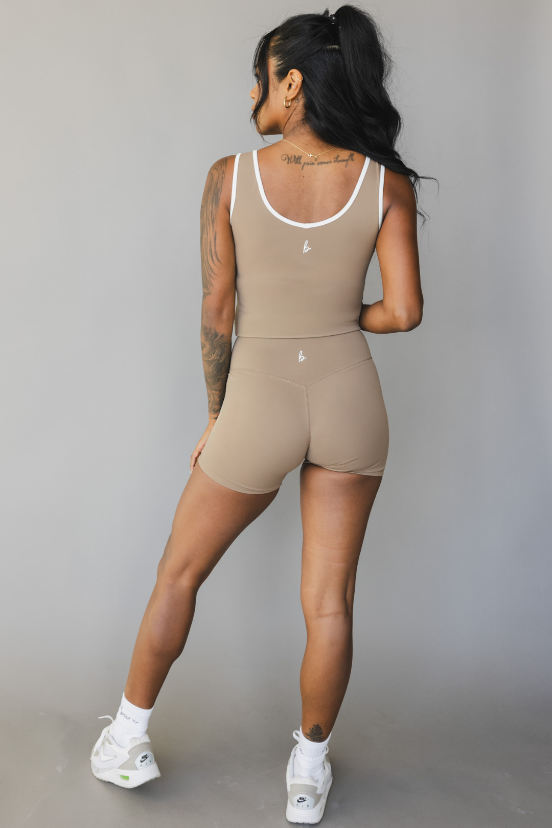 full length back view of a person wearing a tan color athletic tank top with white trim and matching shorts on a gray background