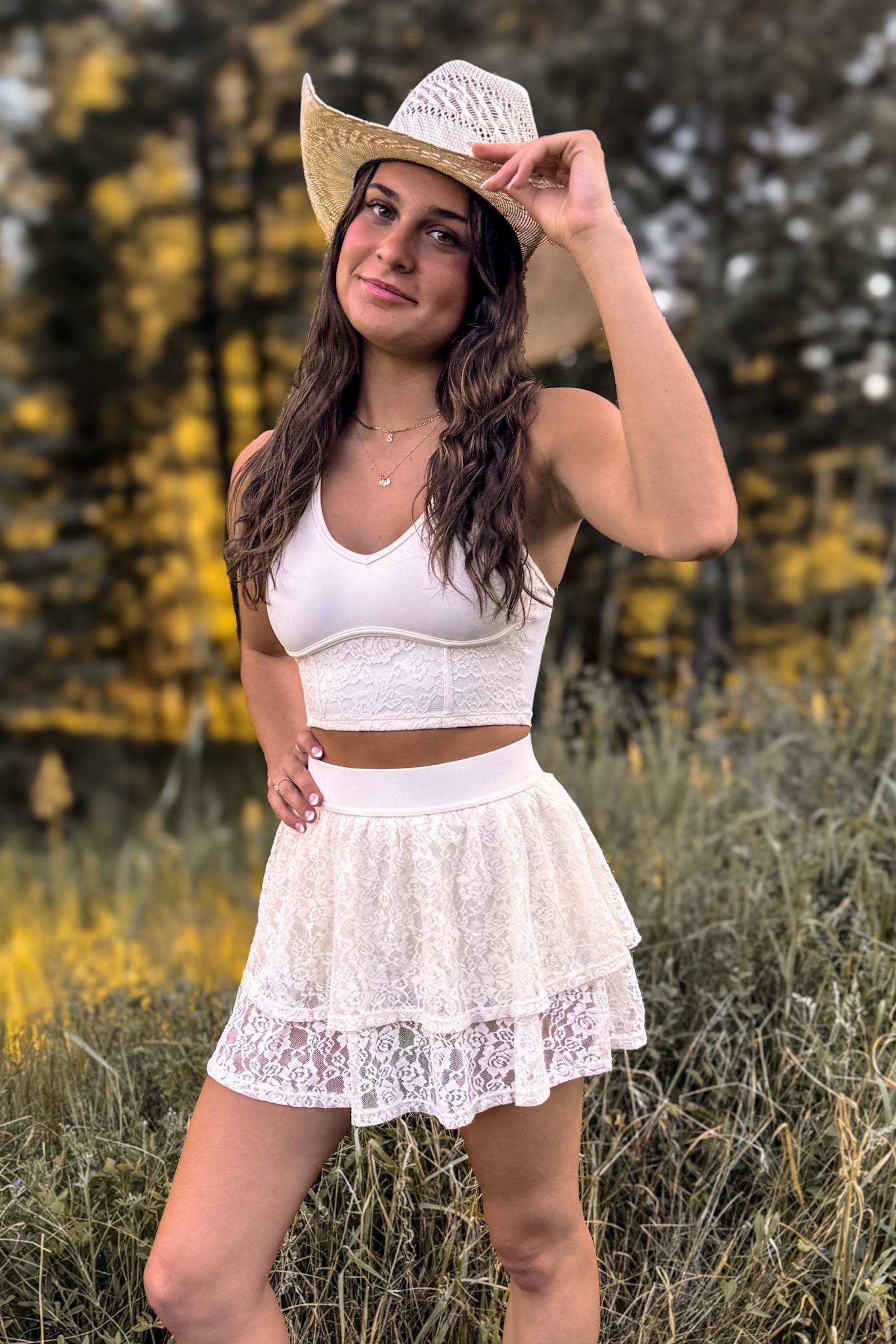 front view of woman wearing a stampede lace active skirt with built-in shorts in cream ivory for festivals and activewear tipping a cowboy hat