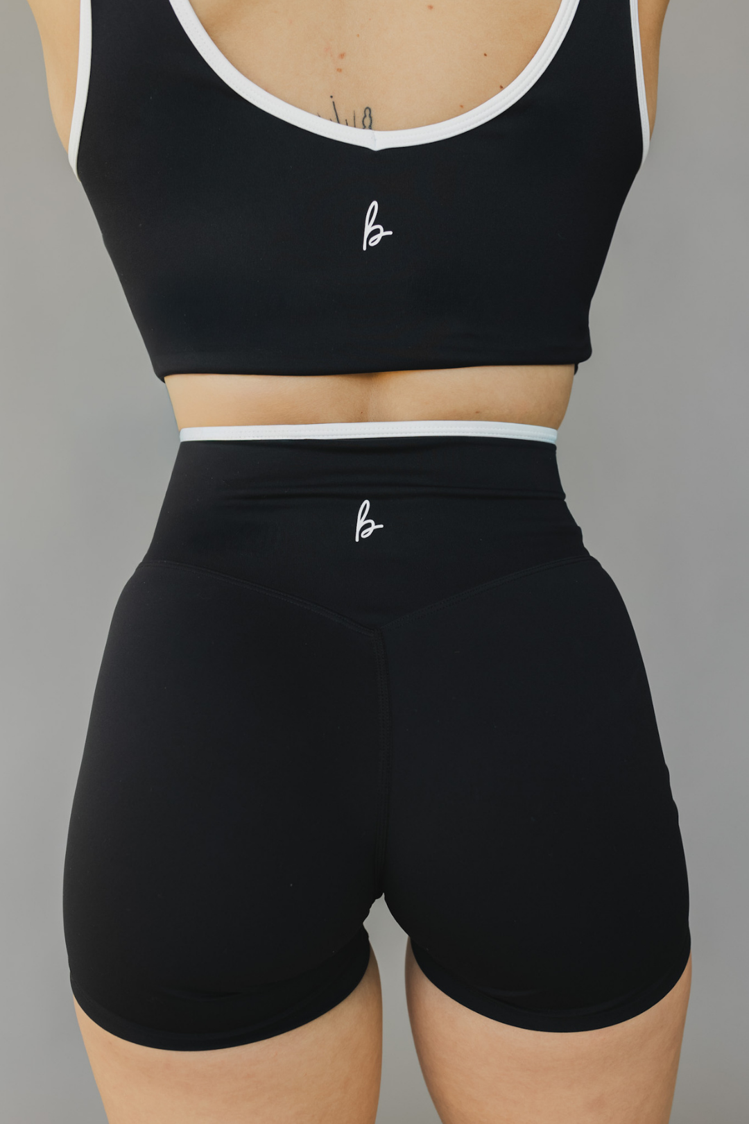 back view of a woman wearing Tina shorts in black with white trim and a matching tank top for athletic wear and loungewear