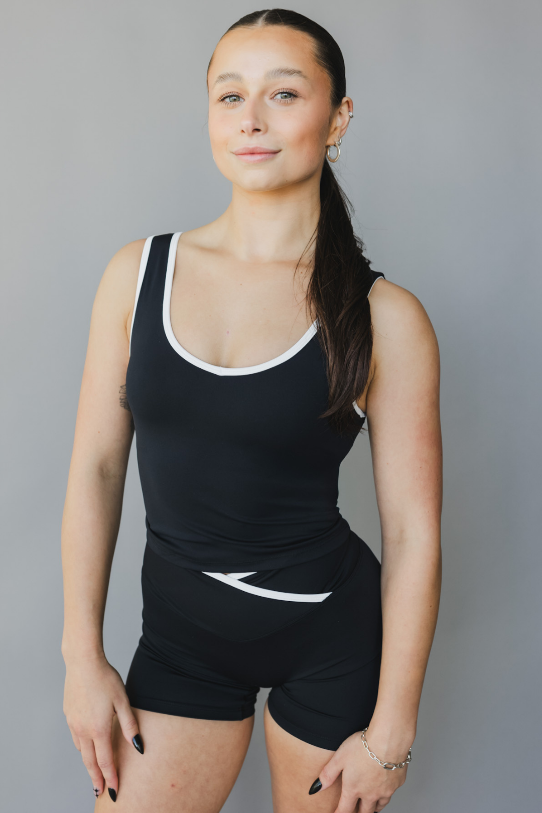 front view of a person wearing a black athletic tank top with white trim and matching shorts on a gray background