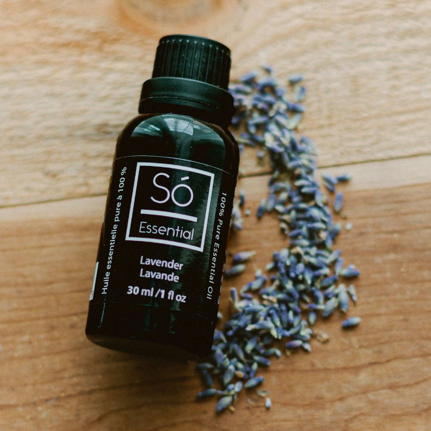 Só Essential lavender essential oil bottle on a wooden surface with scattered lavender flowers.