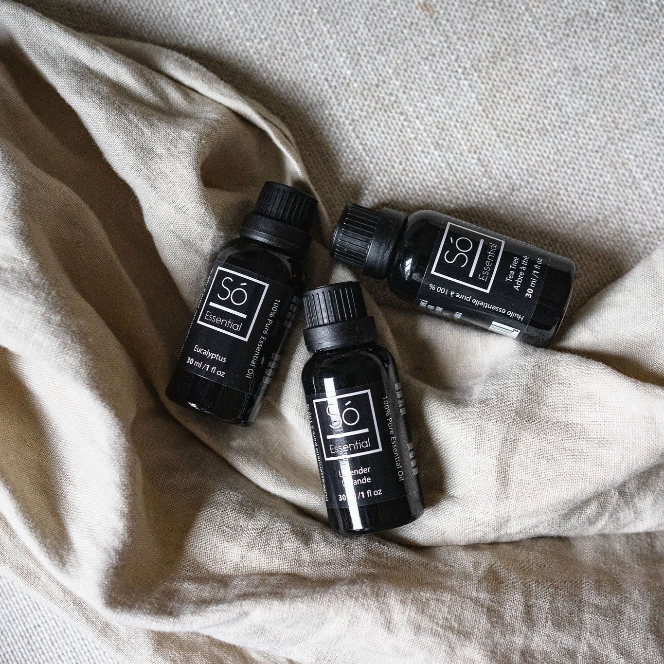 Three black essential oil bottles on a textured beige fabric background