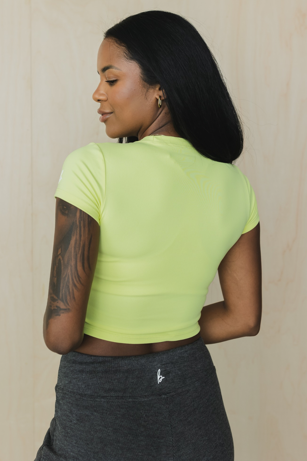 back view of a woman wearing a light green crop top and dark gray pants against a neutral background