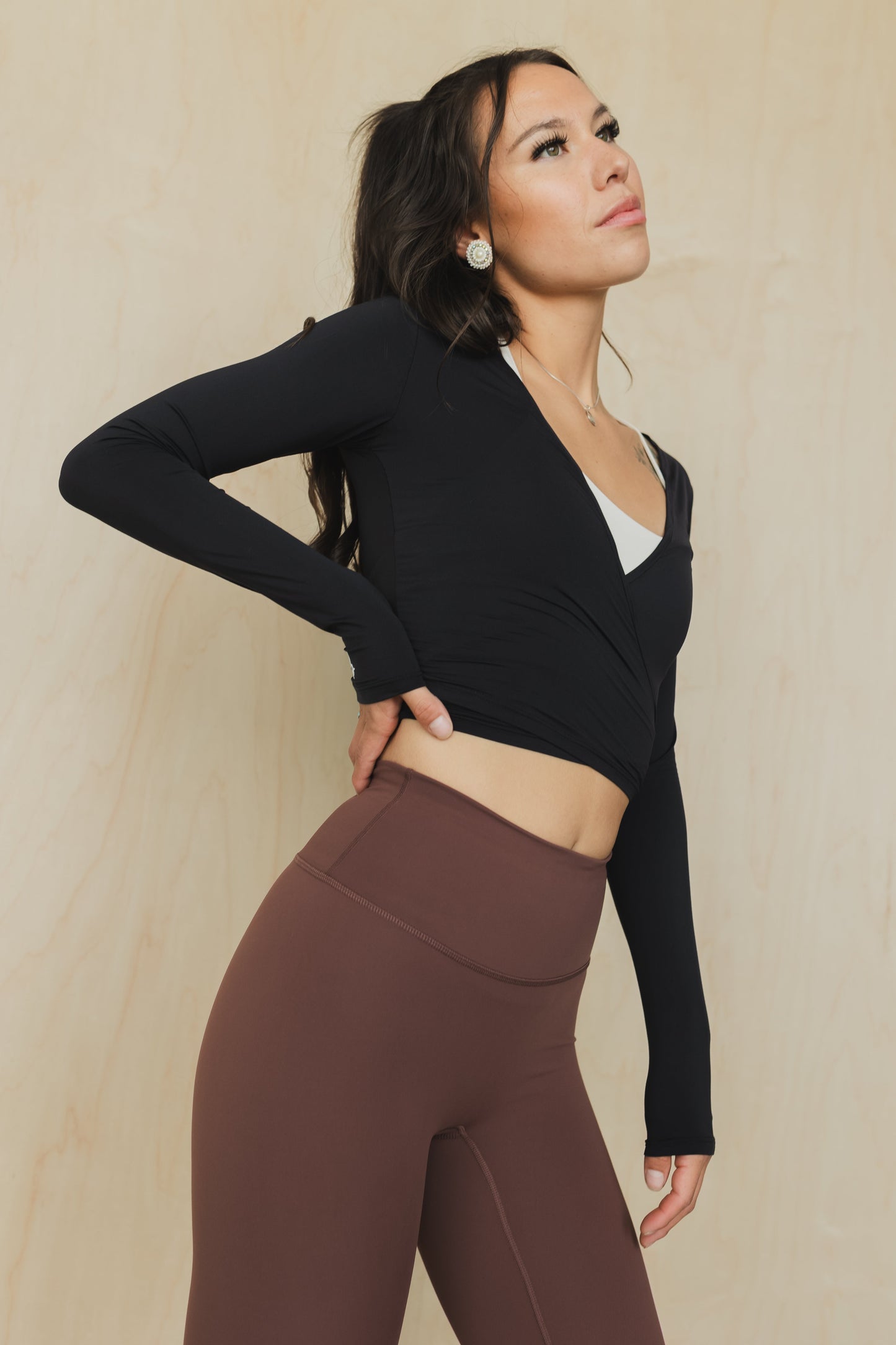 Woman wearing a black long-sleeve top and brown leggings against a beige background