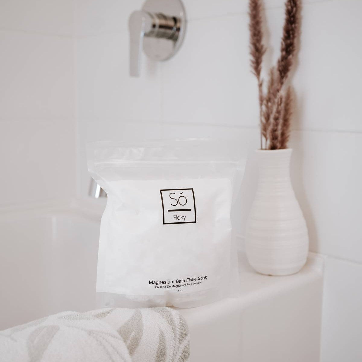 White bag of Só Flaky - Magnesium Bath Soak with branding on a towel in a bathroom setting