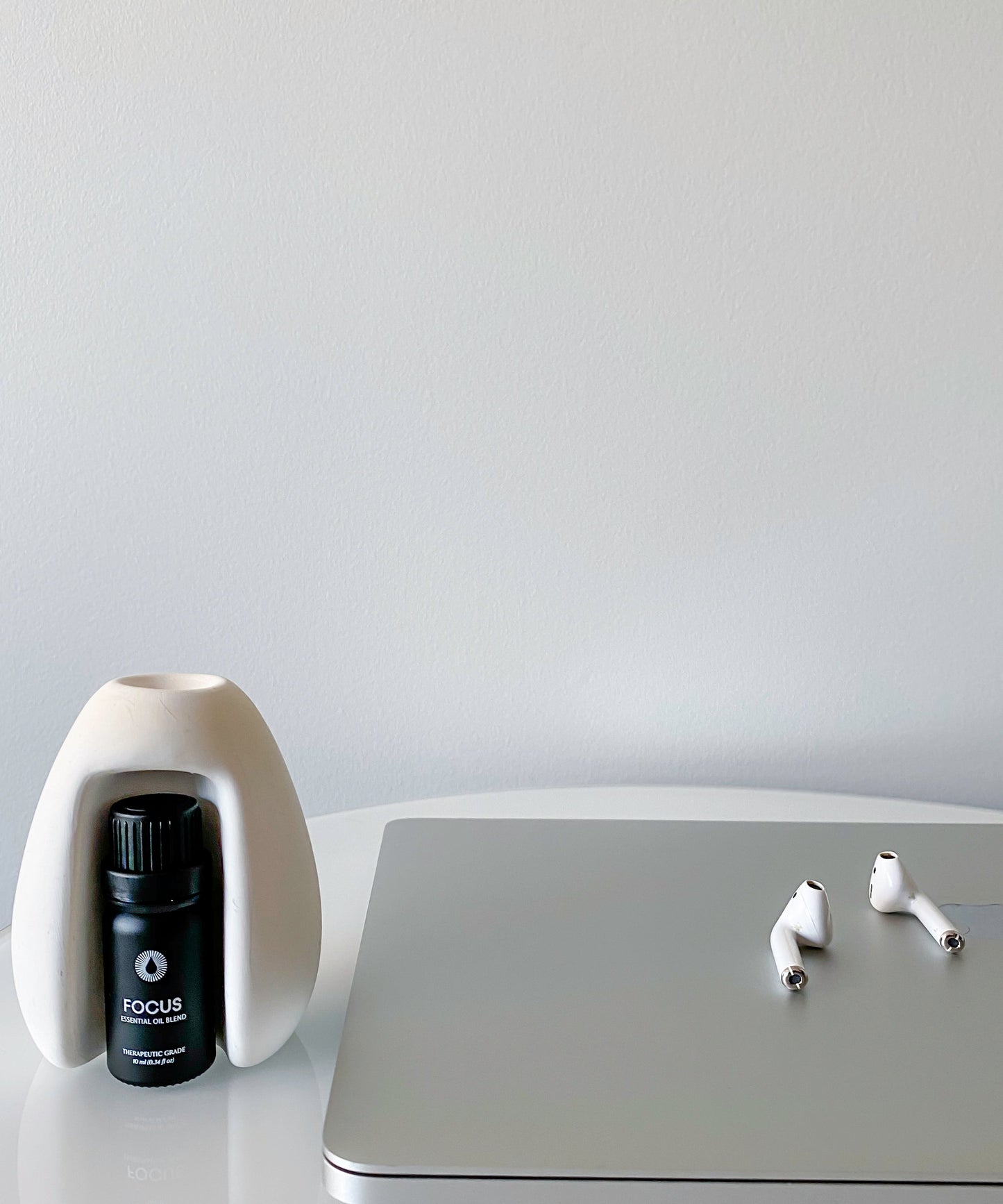 Laptop with earbuds and a focus diffuser kit essential oil aromatherapy set on a white surface.