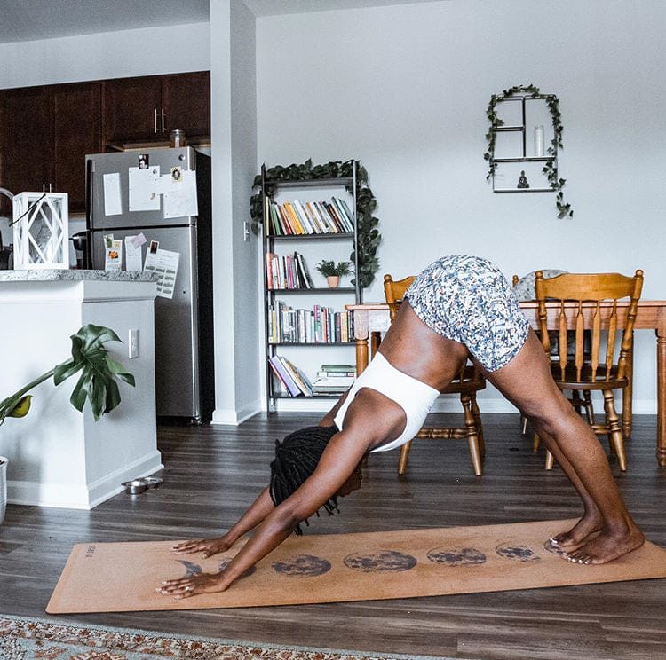 Person doing a yoga pose on a Cork yoga mat with moon phase design  with kitchen and dining area in the background.
