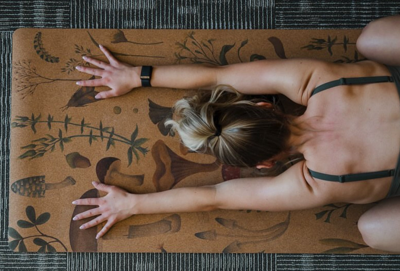 Person practicing yoga on a cork mat with mushroom and plant design