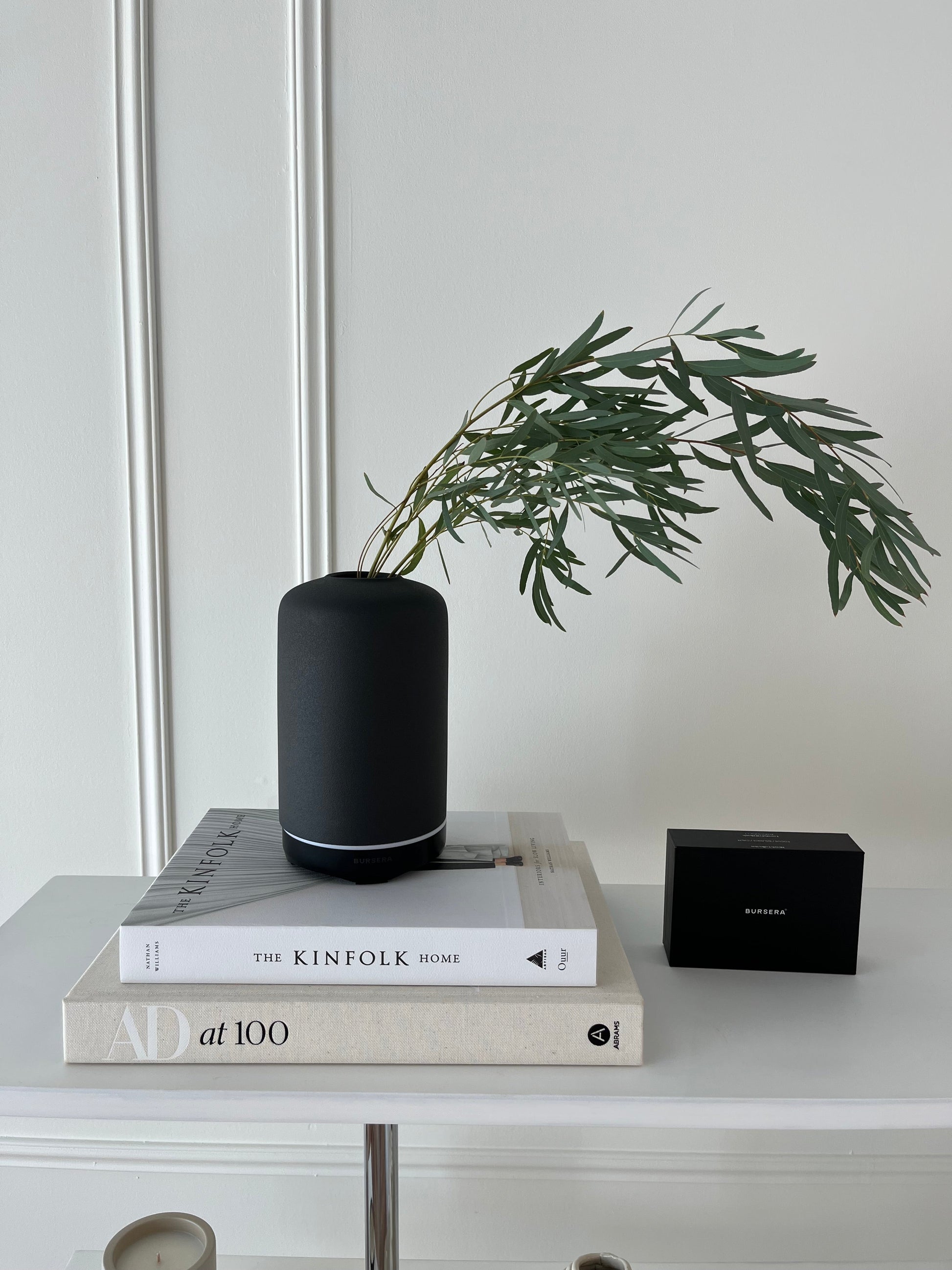 ash essential oil diffuser aromatherapy home decor on books with a plant and electronic device in the background