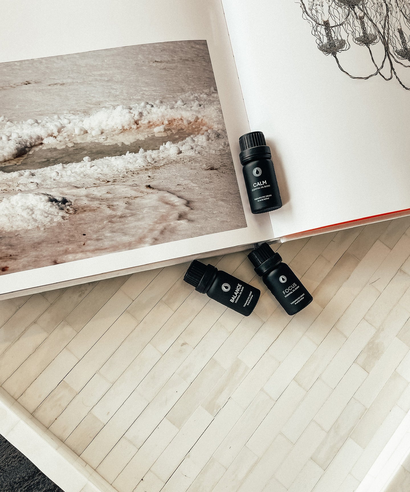 Four black essential oil bottles on a wooden surface with a magazine in the background.