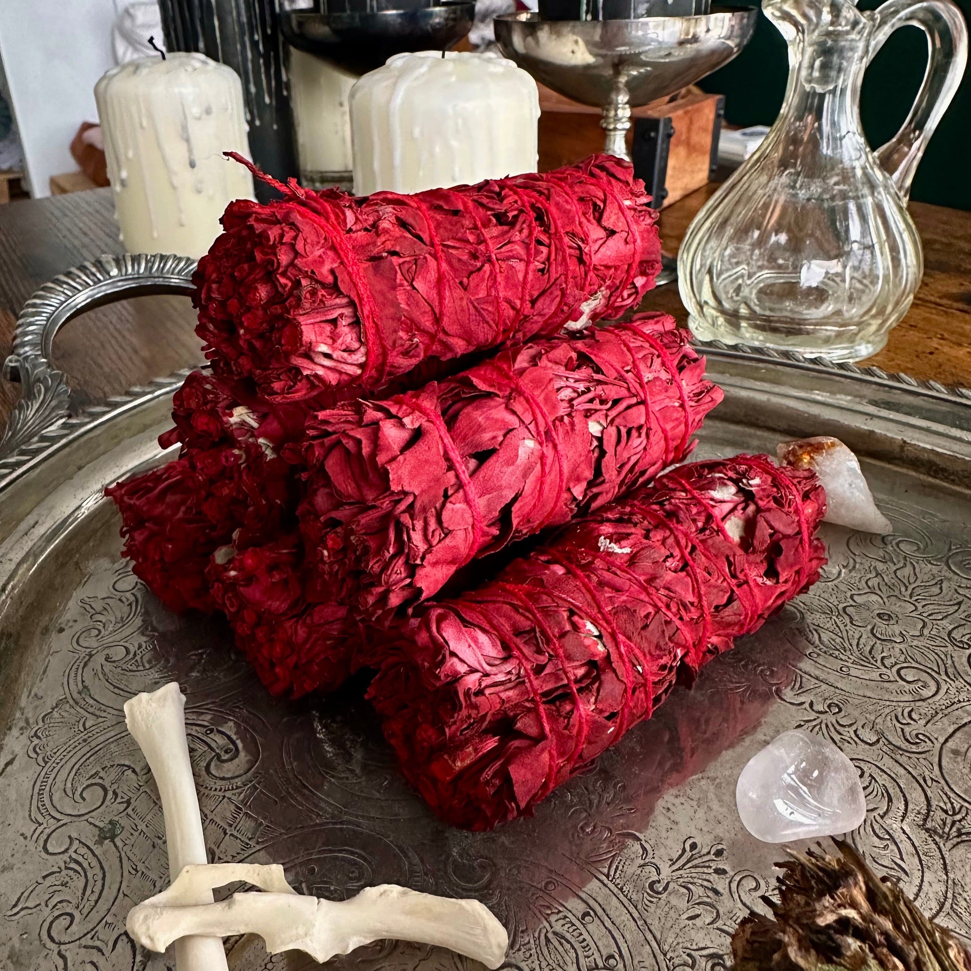 Three red smudge sticks on a decorative metal tray with candles and a vase in the background.