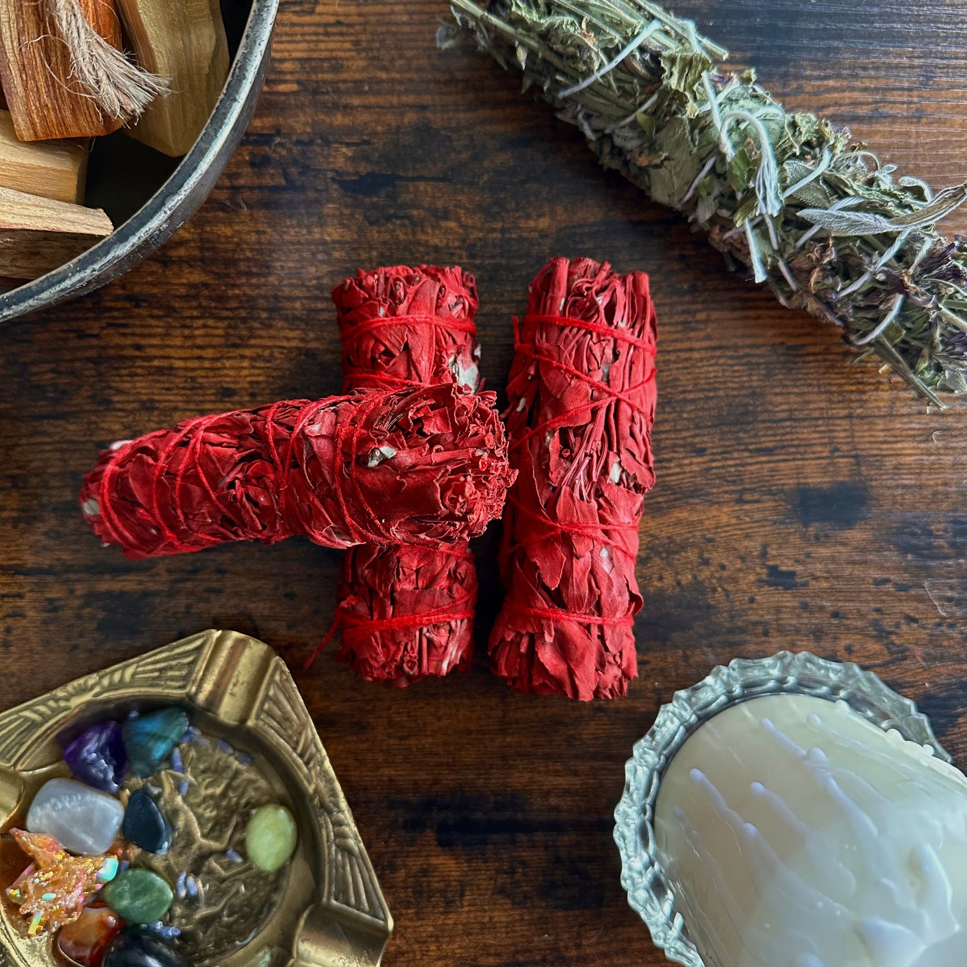 Red sage wrapped bundles on a wooden surface with crystals and a candle.
